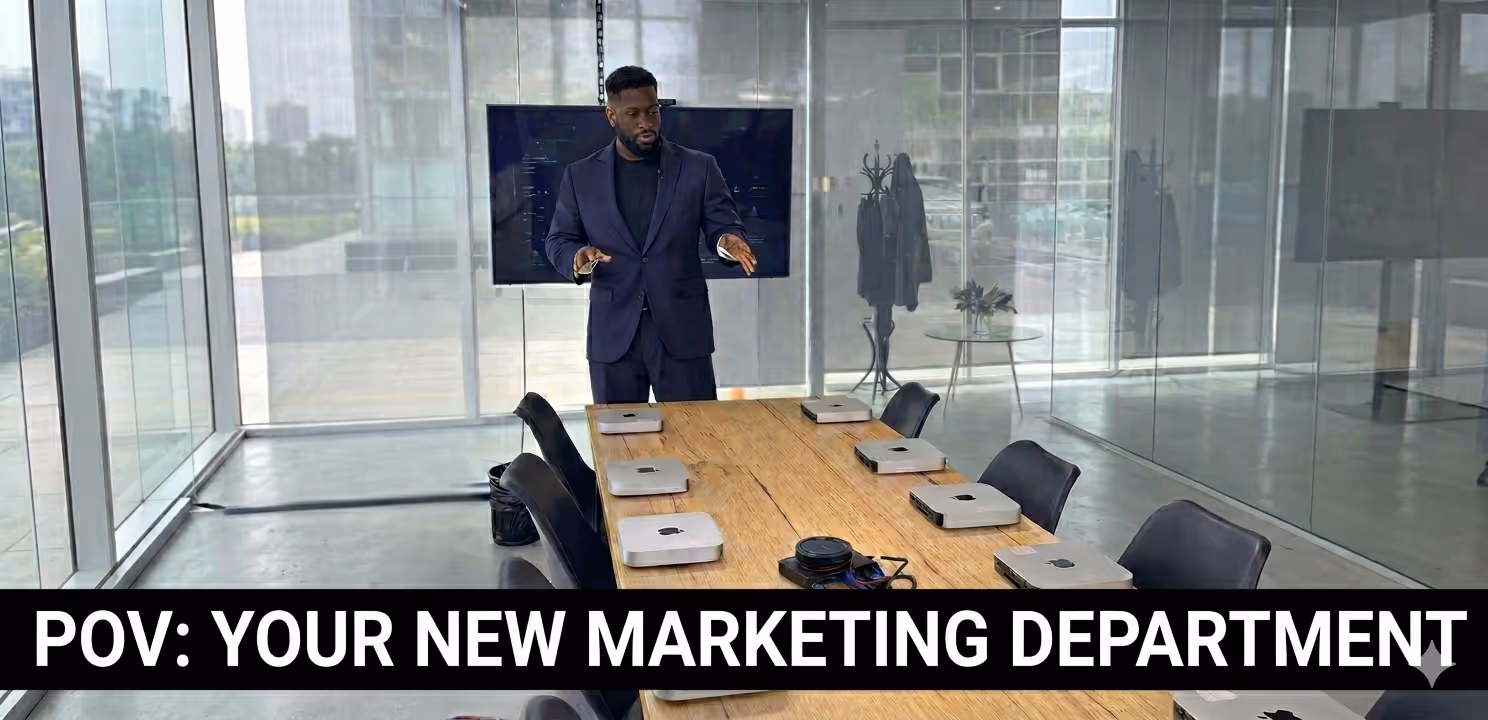 Man in dark suit standing at end of conference table with six laptops in a modern glass-walled office, captioned 'POV: YOUR NEW MARKETING DEPARTMENT.'