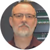 Middle-aged man with glasses and a short gray beard in front of a bookshelf filled with books.