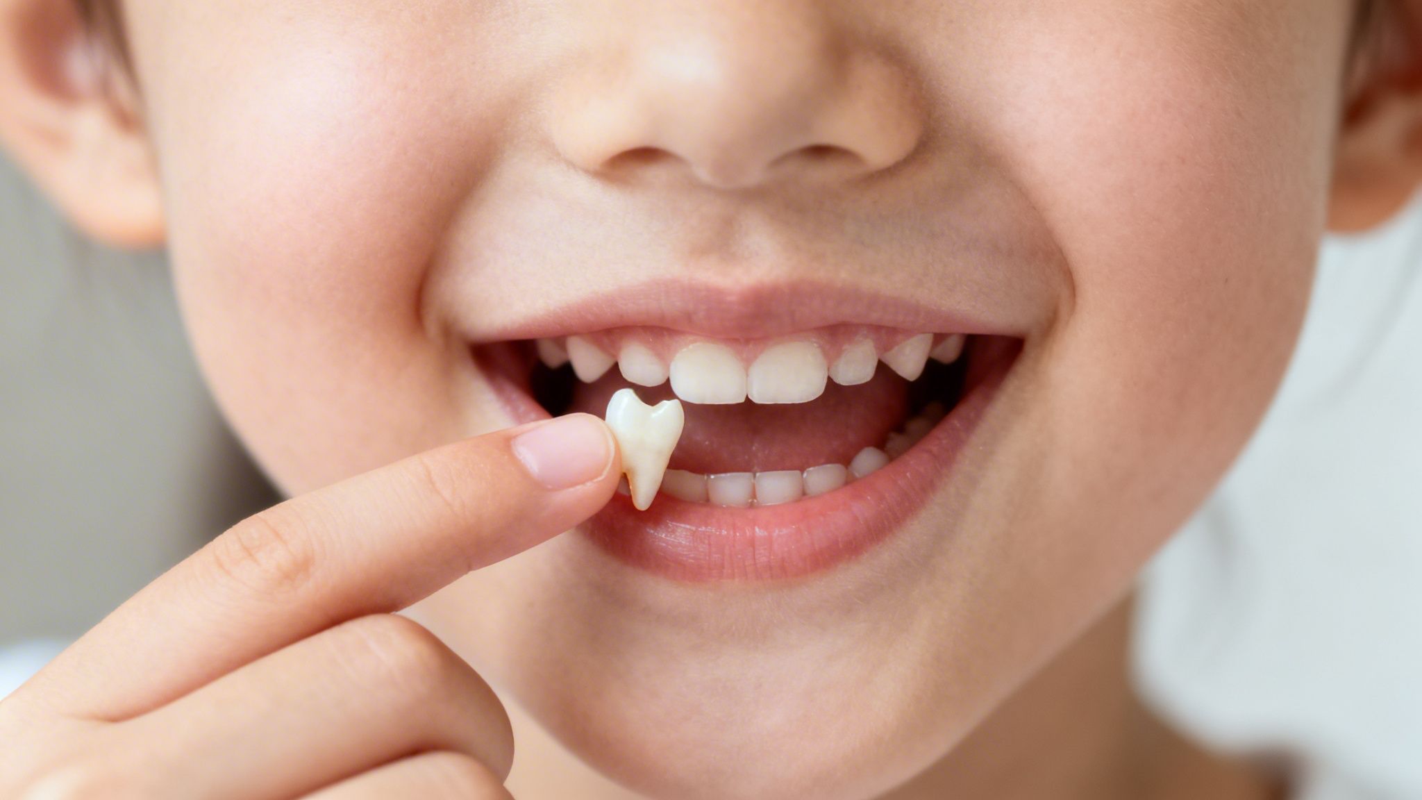 A happy child proudly smiles, holding up a recently lost white baby tooth.
