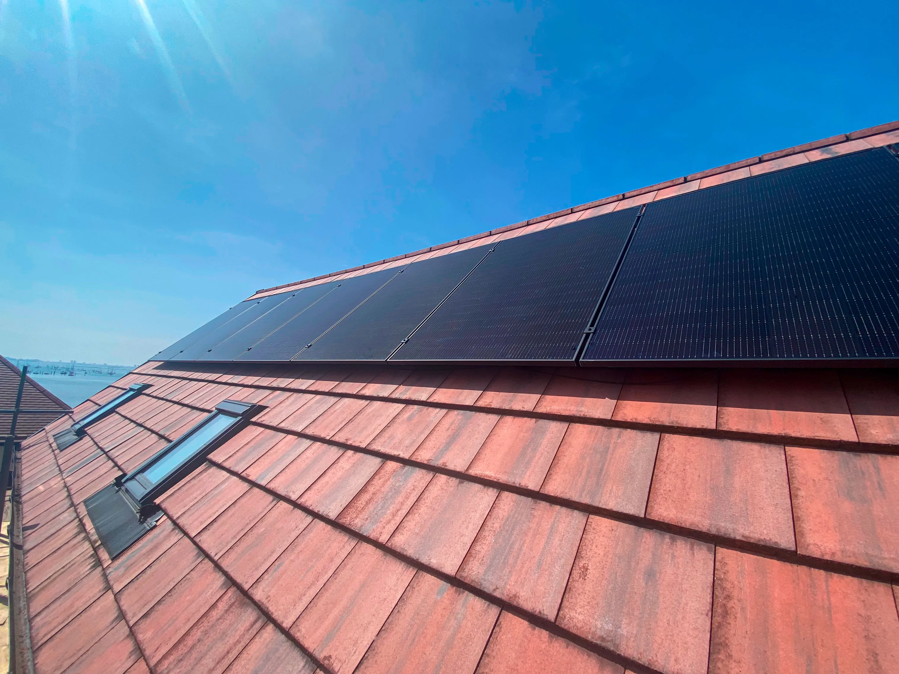 Eight solar panels installed on a red tiled roof under a bright blue sky.