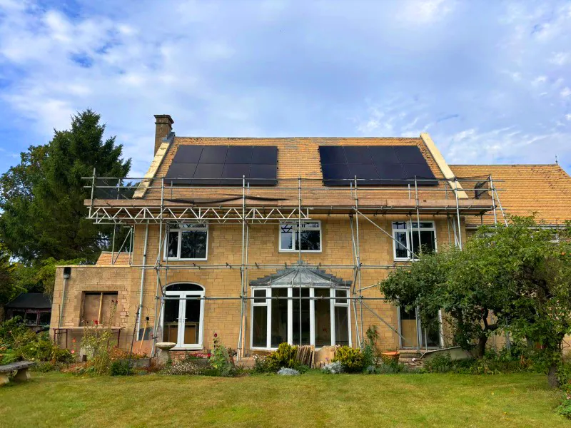 Cotswold stone house with scaffolding and solar panels installed on the roof
