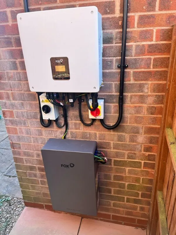 Wall-mounted Fox inverter and battery system with connected electrical wires against a brick wall.