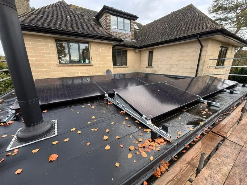 Black solar panels installed by MakeMyHouseGreen on a flat roof with autumn leaves scattered around