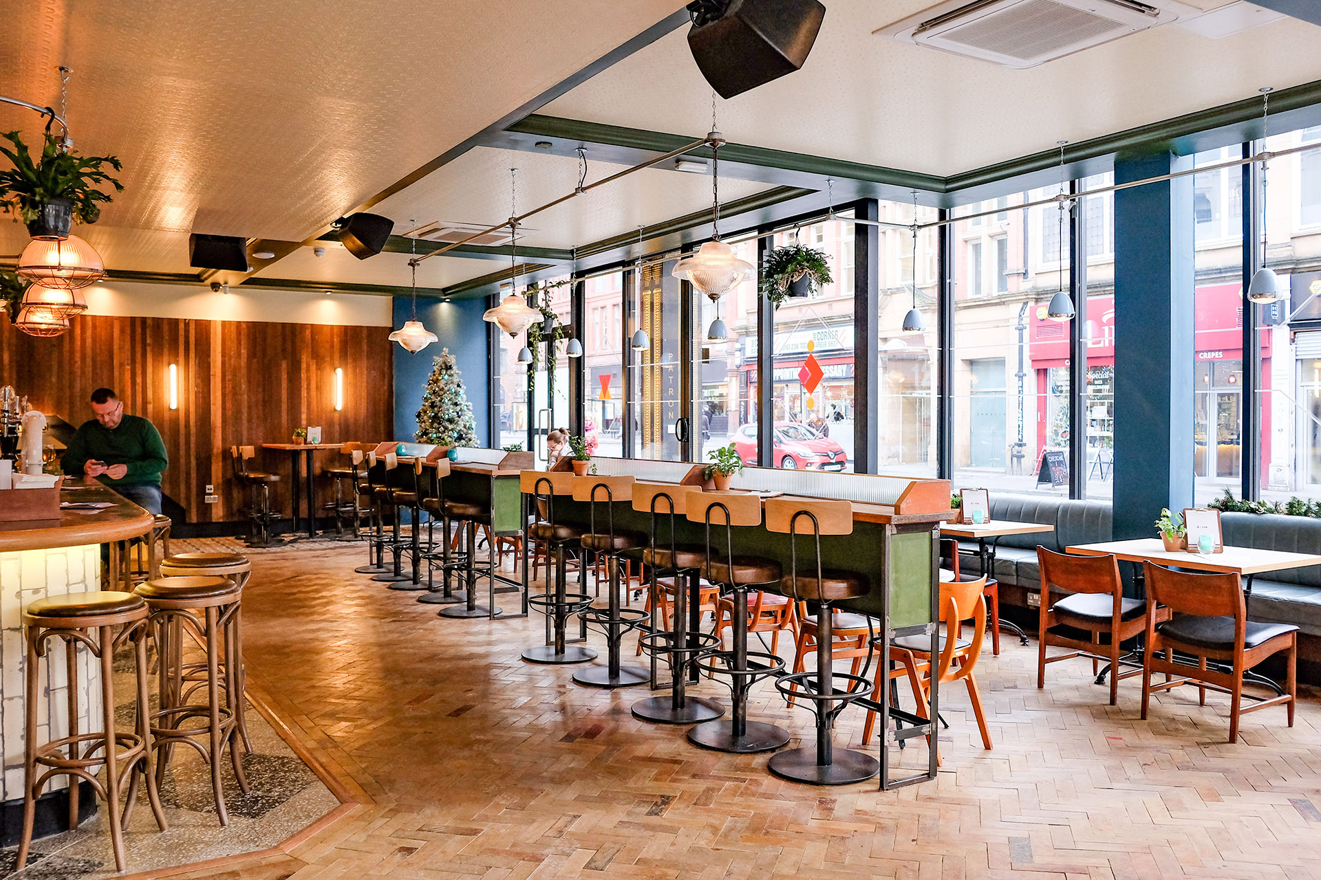 Interior of The Patron with seating, a man at the bar and window graphics looking out onto the Northern Quarter.