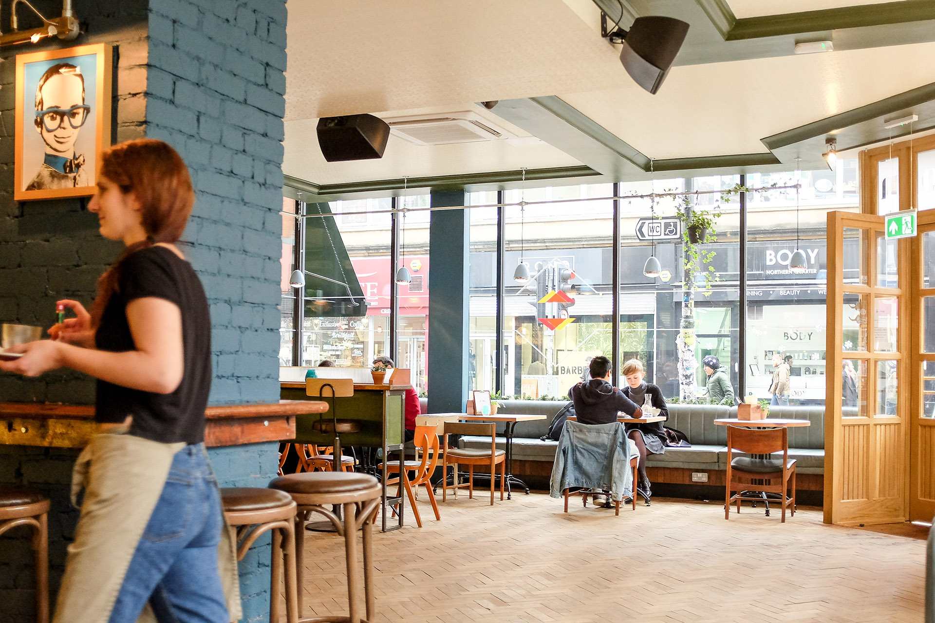 A waitress walks carrying two plates, while a couple eats in the background.