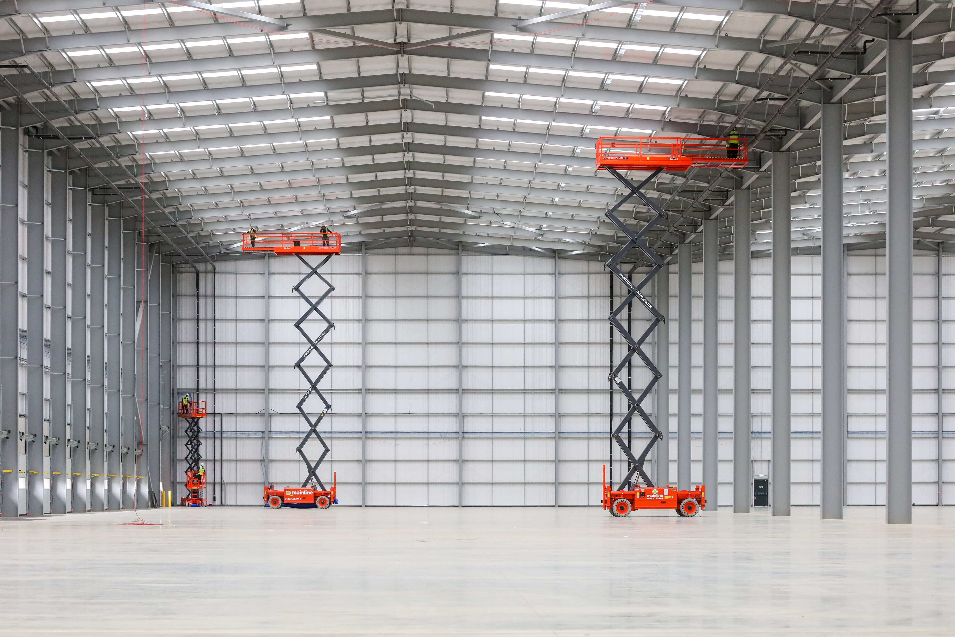 People standing on two scissor lifts inside a large warehouse.