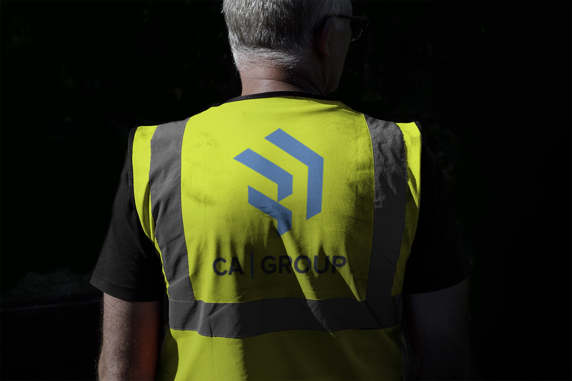 A man standing with his back to the camera, wearing a high-visibility jacket with the CA Group logo.