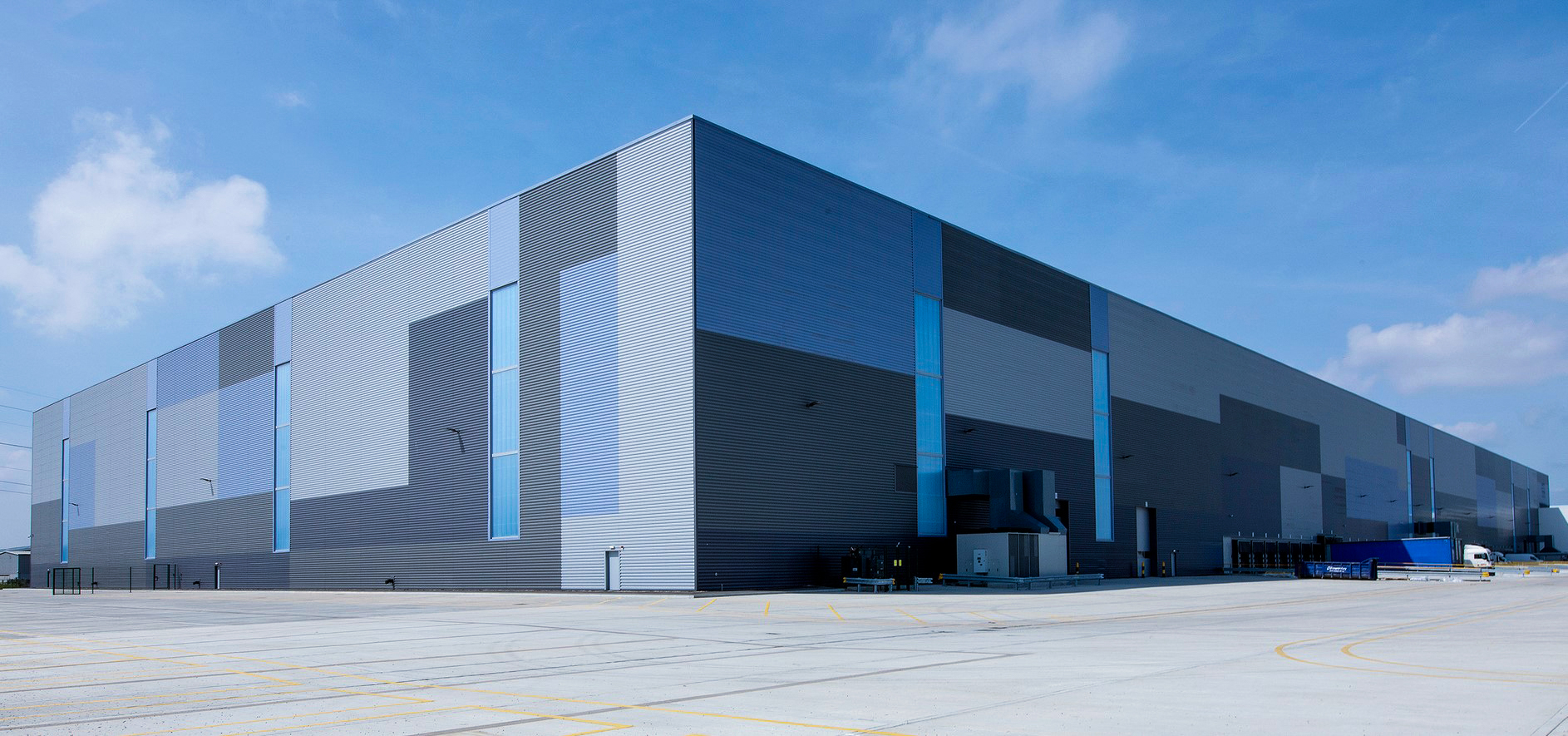A large building with blue and grey cladding, set against a blue cloudy sky.
