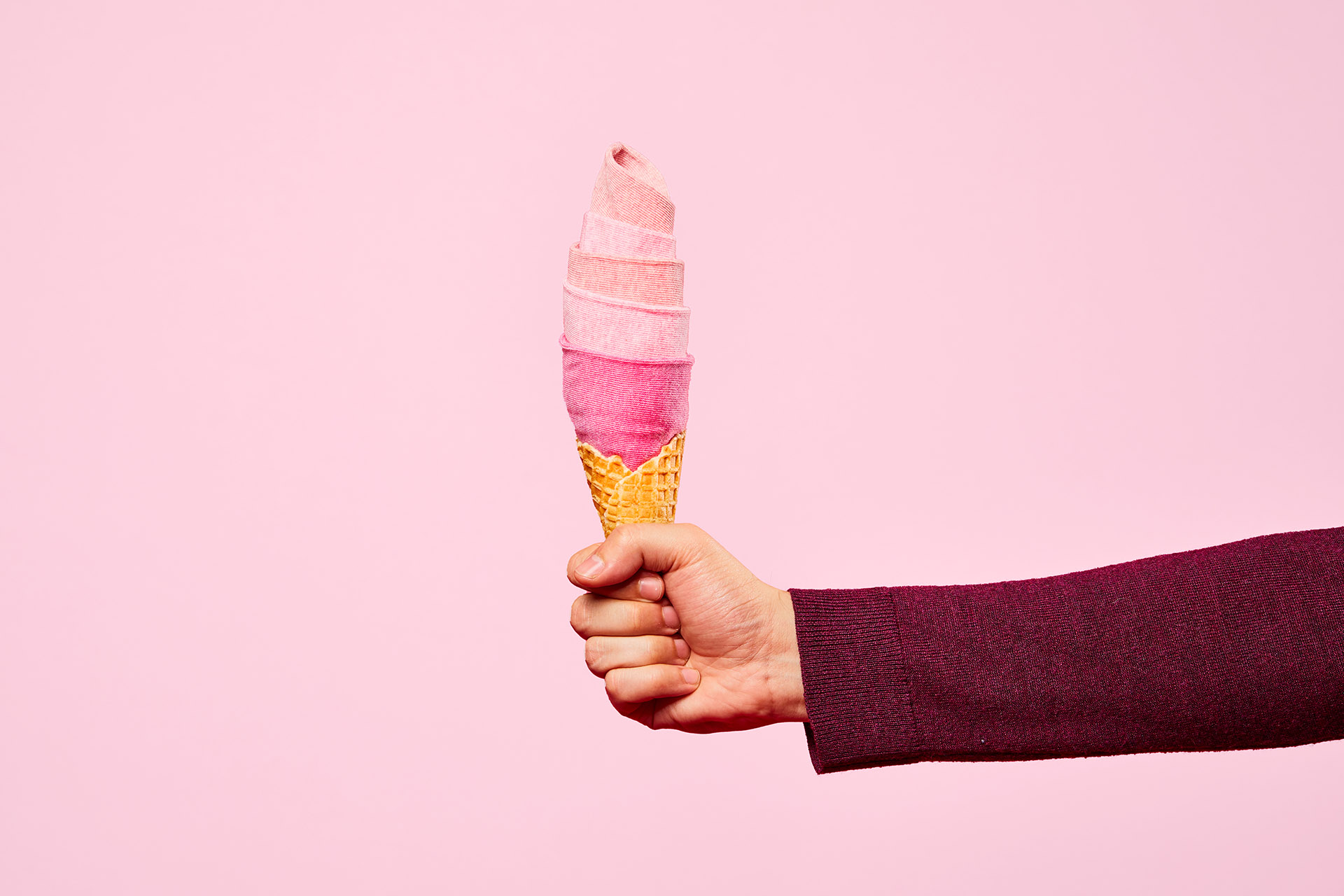 An arm holds an ice cream cone topped with pink socks to resemble ice cream, against a pink backdrop.