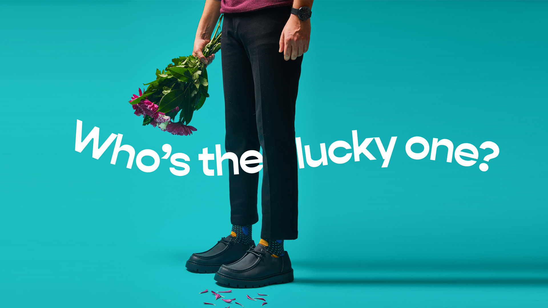 Man's lower body in black trousers and polka-dot socks holding flowers, with text 'Who's the lucky one?' on a turquoise background.