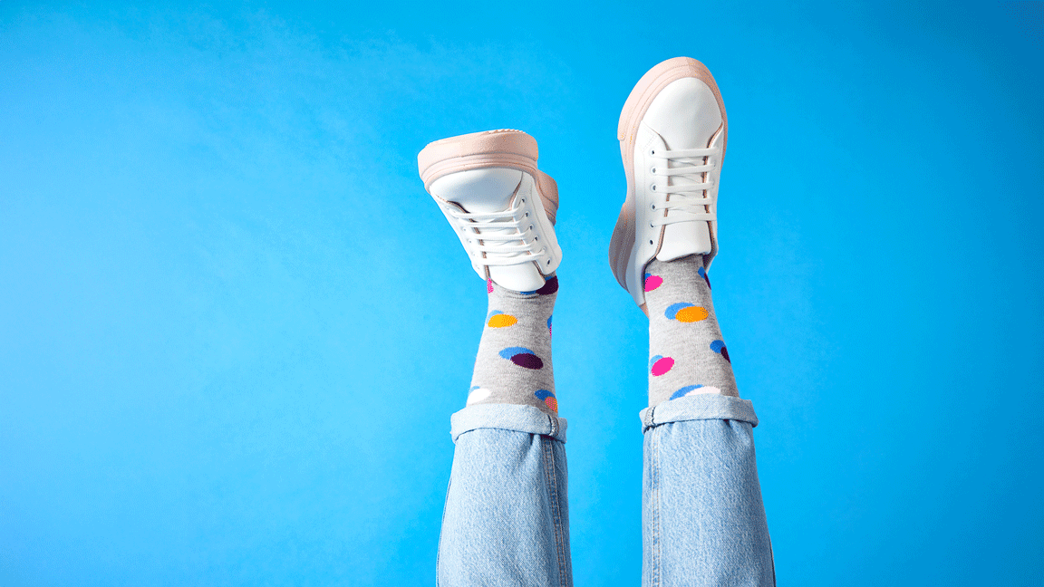 Legs wearing grey socks with multicoloured polka dots moving side to side on a light blue background.