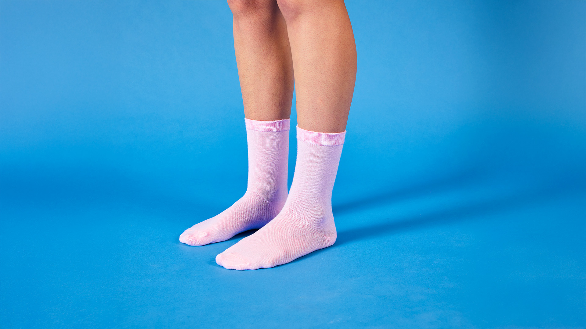Close-up of a woman's legs wearing baby-pink socks on a light blue background.