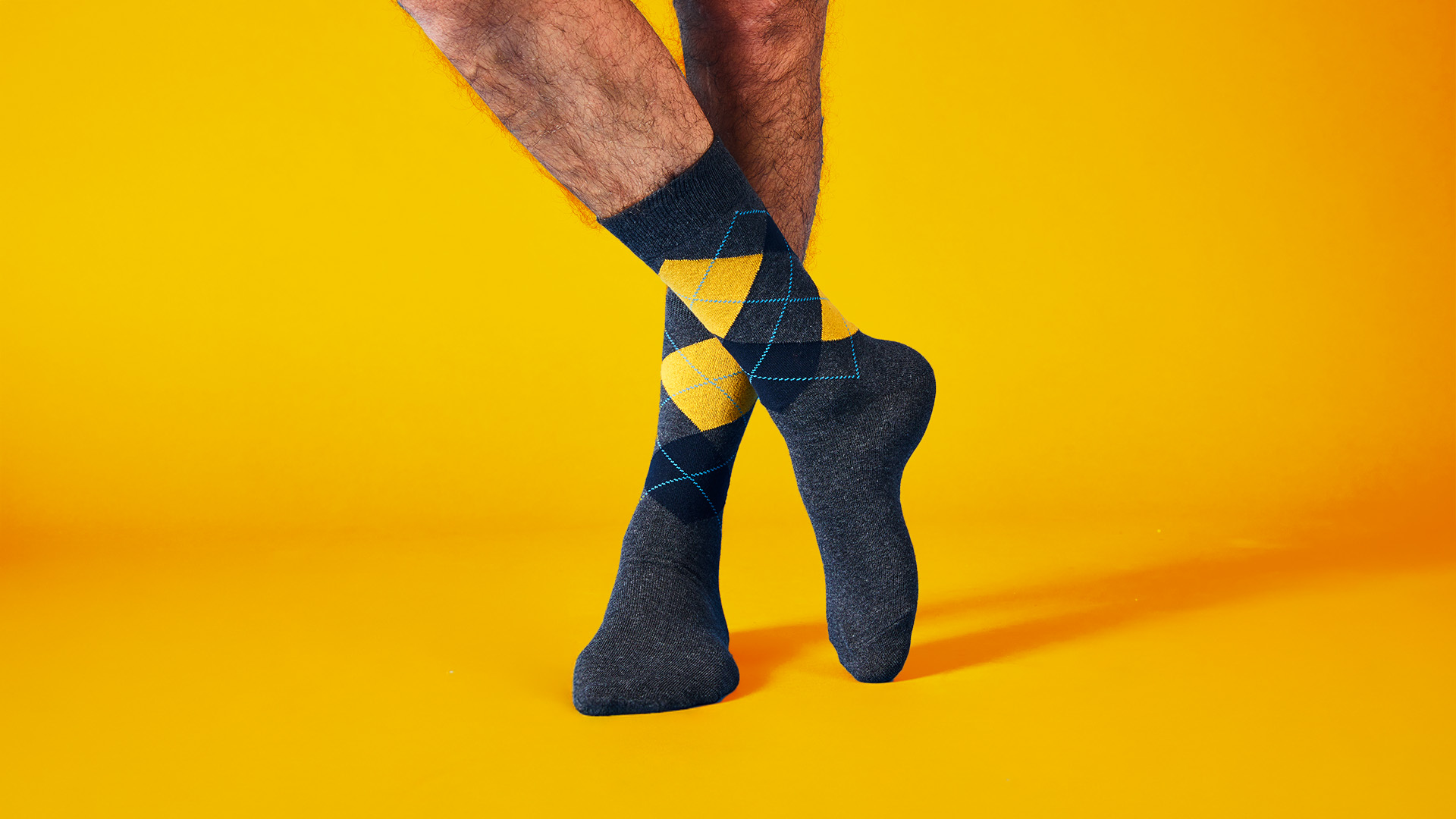 Close-up of a man's legs wearing dark grey socks with yellow diamonds and blue lines on a yellow background.