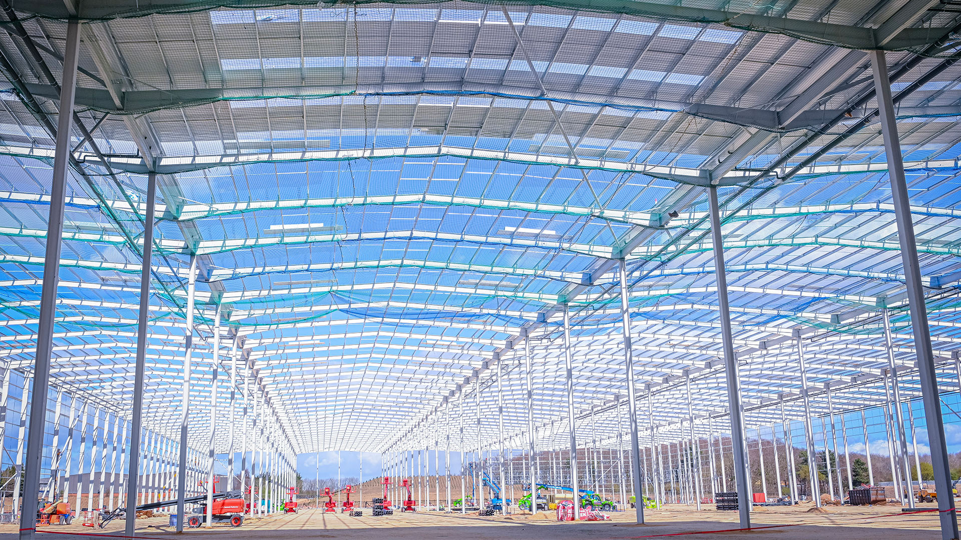 Wide shot of an industrial building under construction, with machinery in the background and safety netting on the roof.