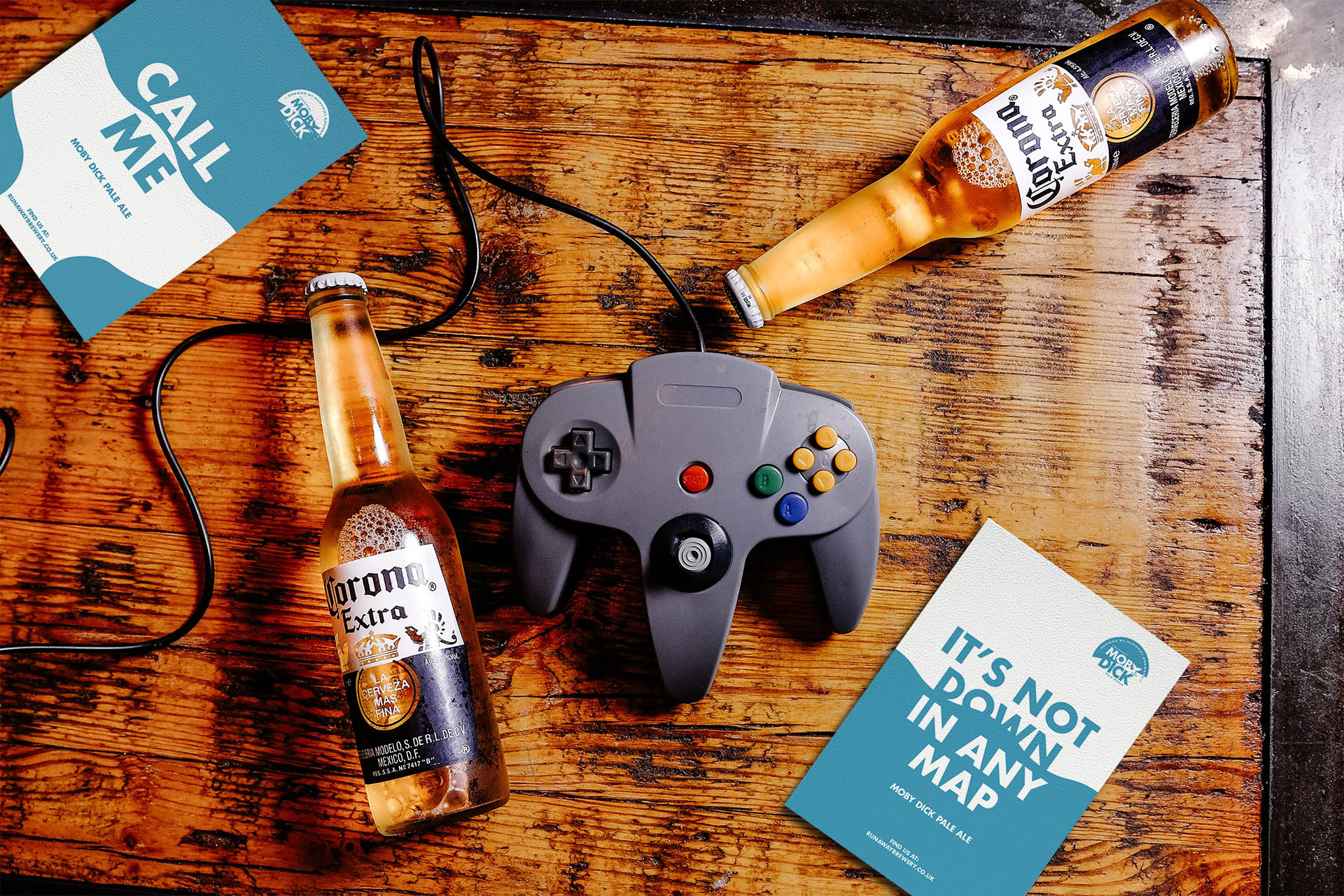 Bird’s-eye view of a wooden table with flyers, a Nintendo controller and two bottles of Corona beer.