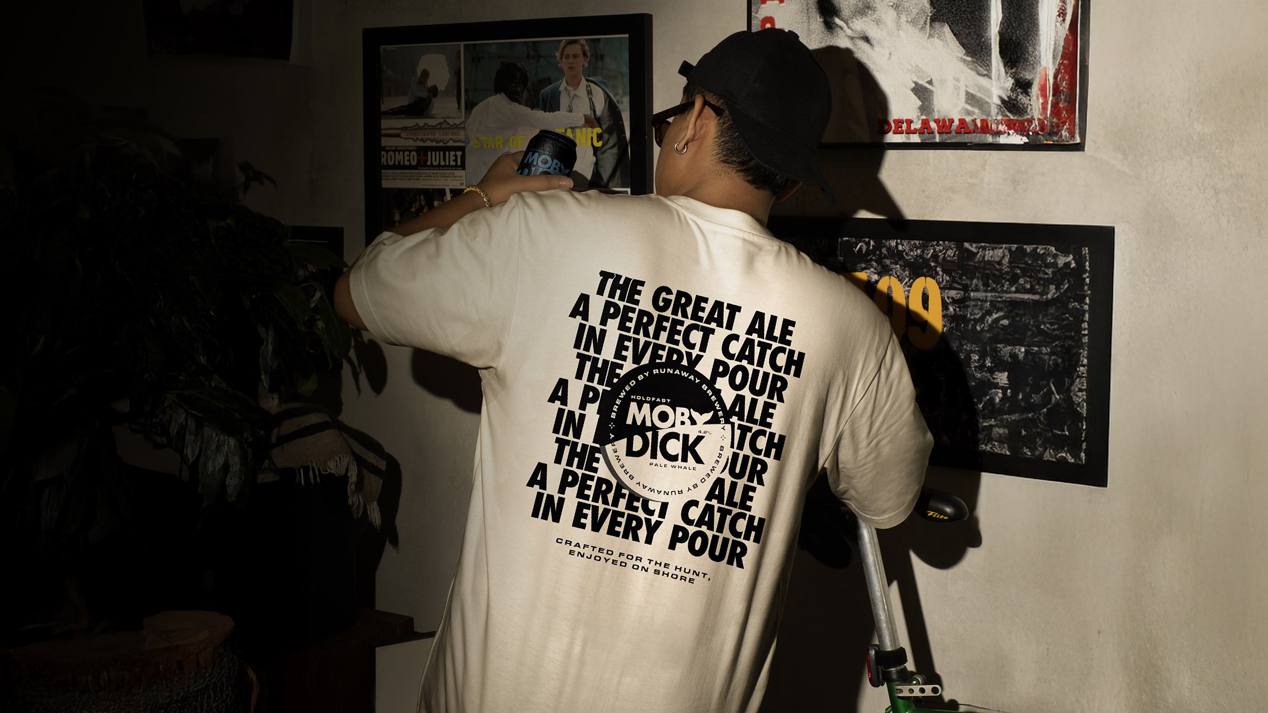 A man with his back to the camera wears sunglasses, a black baseball cap and a white t-shirt with Moby Dick branding.