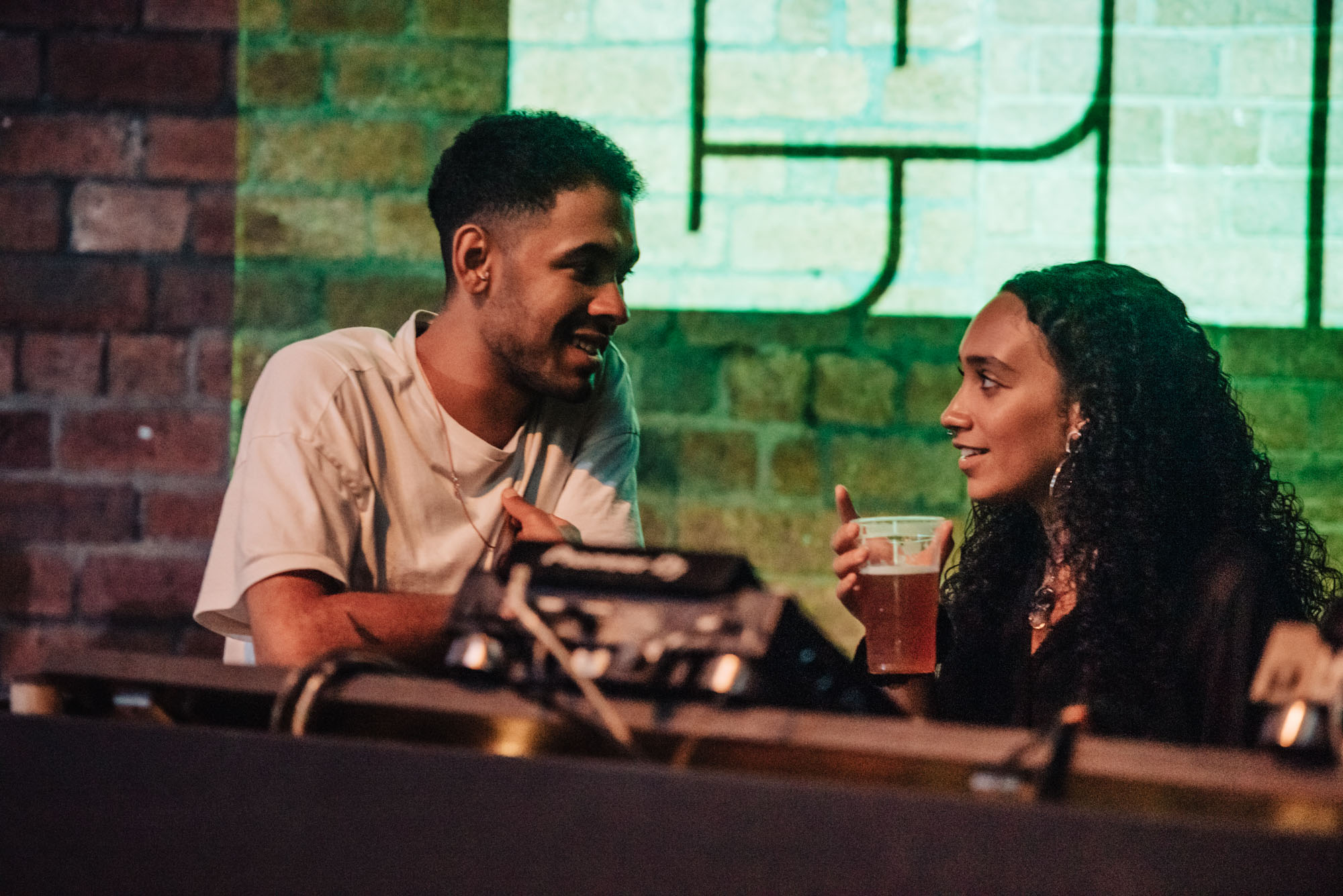Two people talking at the DJ booth in a bar.