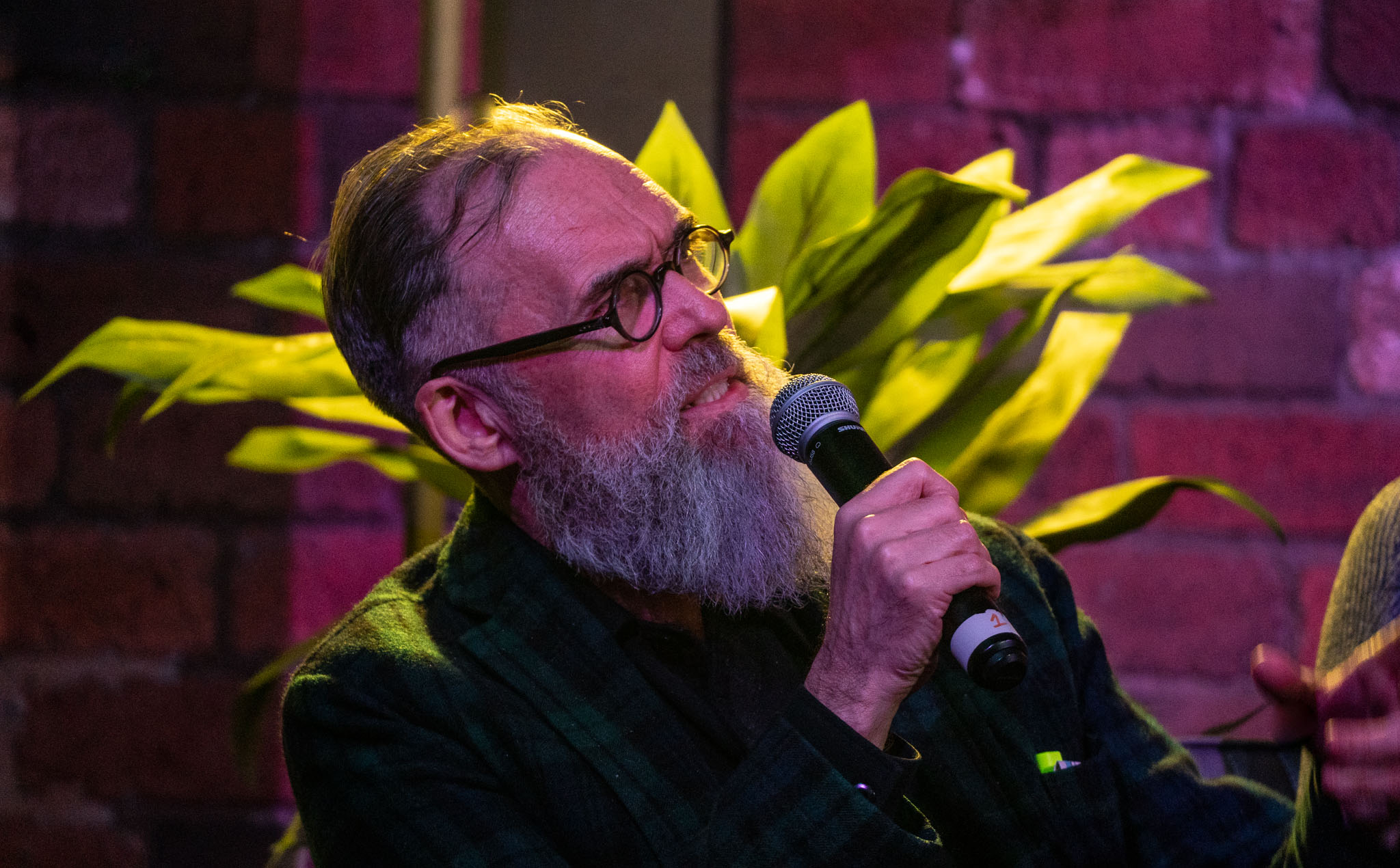 Close-up of a fashionable older man with a beard and glasses speaking into a microphone.