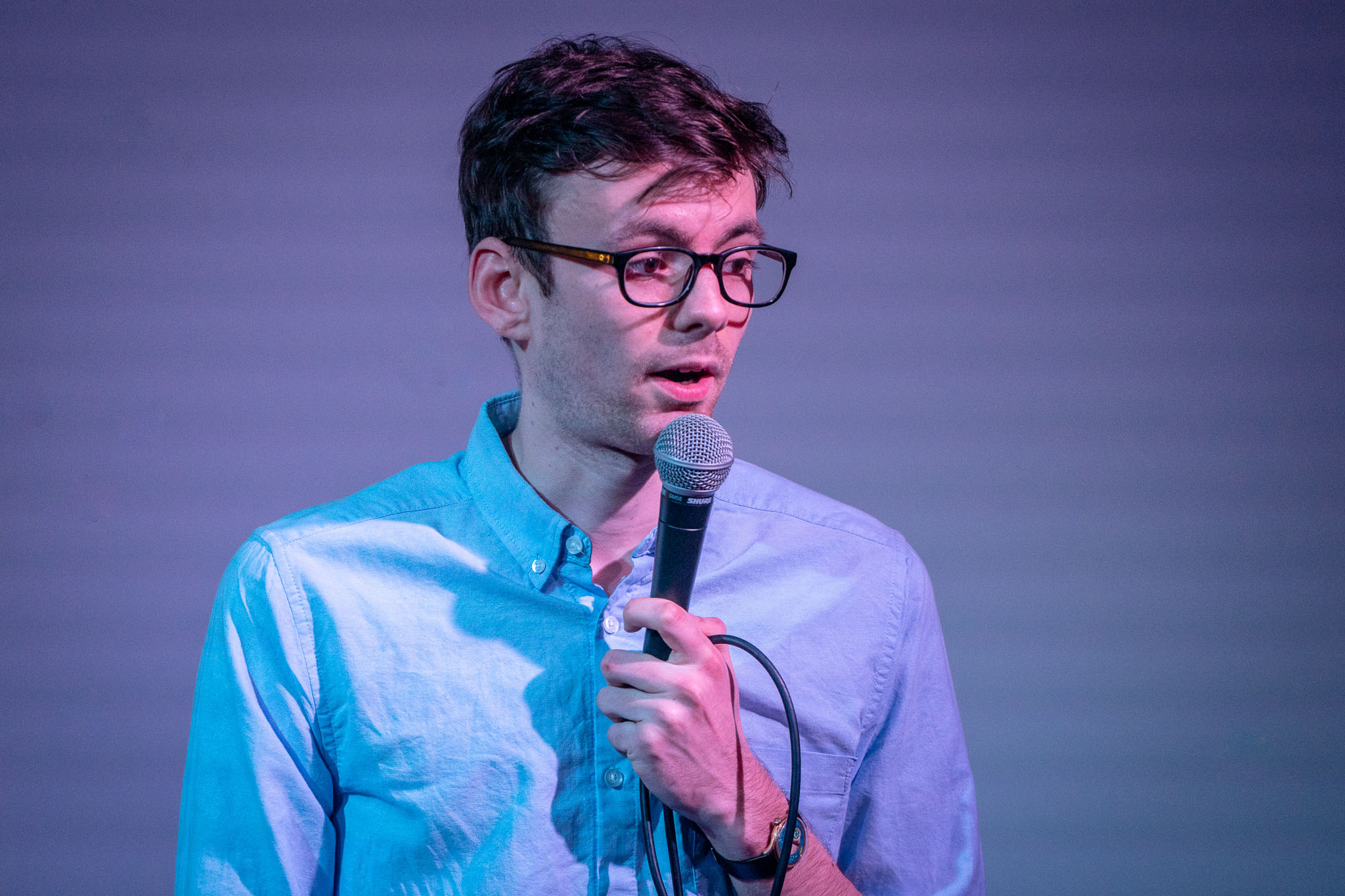 Close-up of a man wearing glasses, speaking into a microphone.