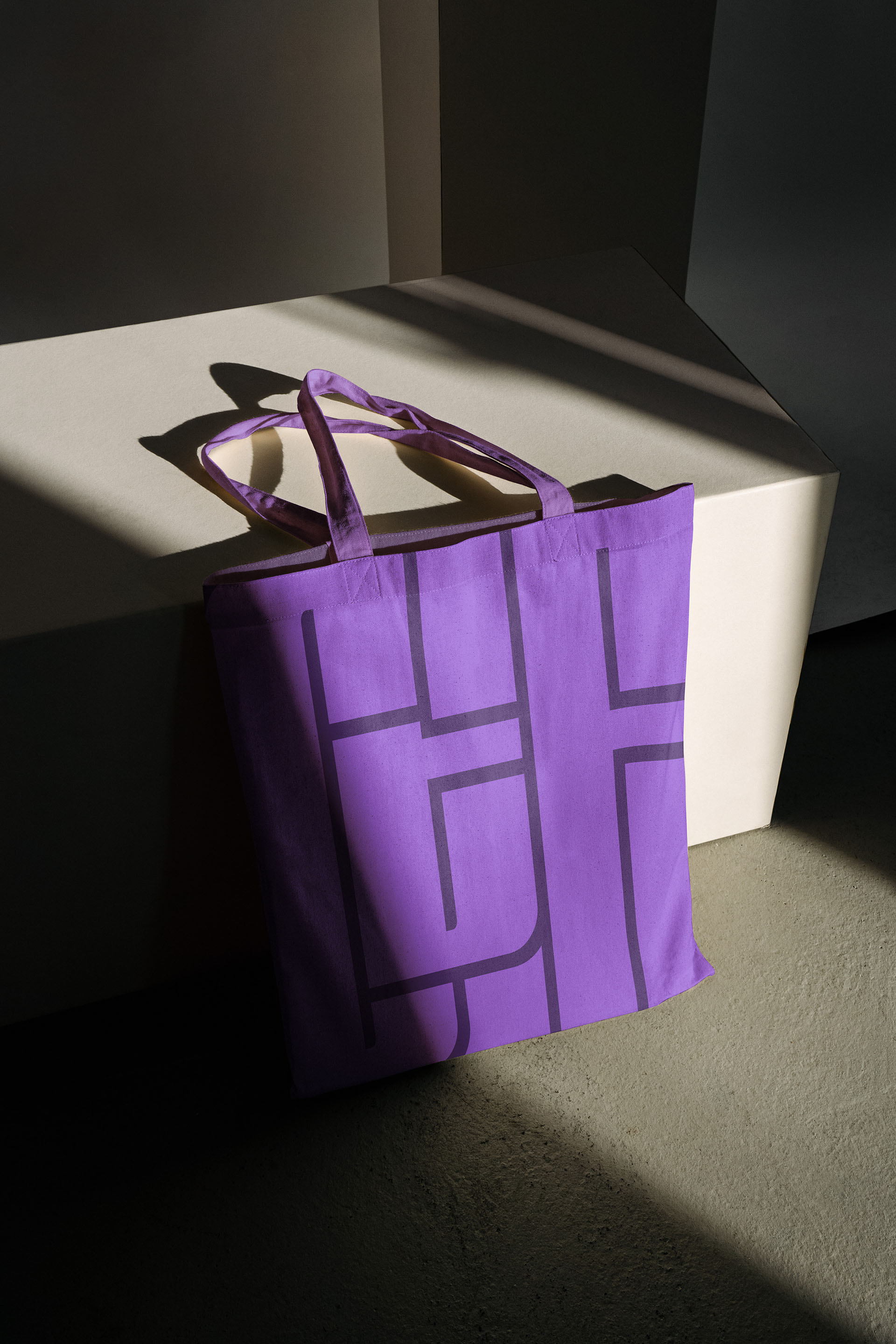 A Chew the Fat purple tote bag leans against a white wall.
