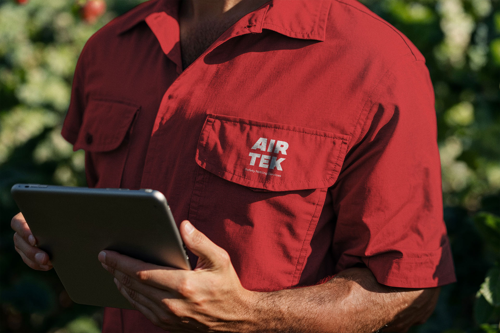 A man wearing a red short-sleeved shirt with the Airtek logo in white on the pocket holds an iPad.