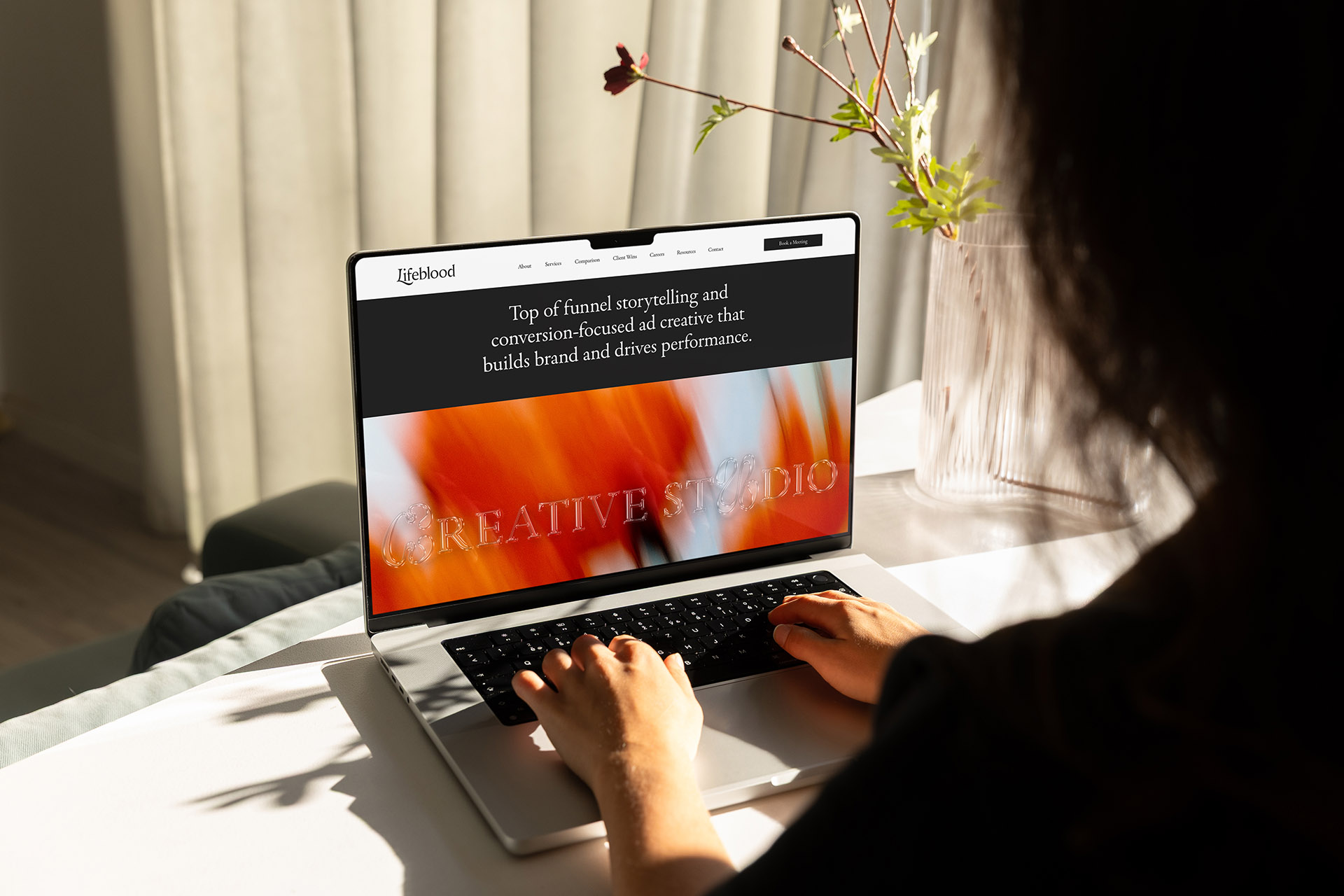 A women is using a laptop on a white table showcasing a website designed by Rootin' Tootin' studio.