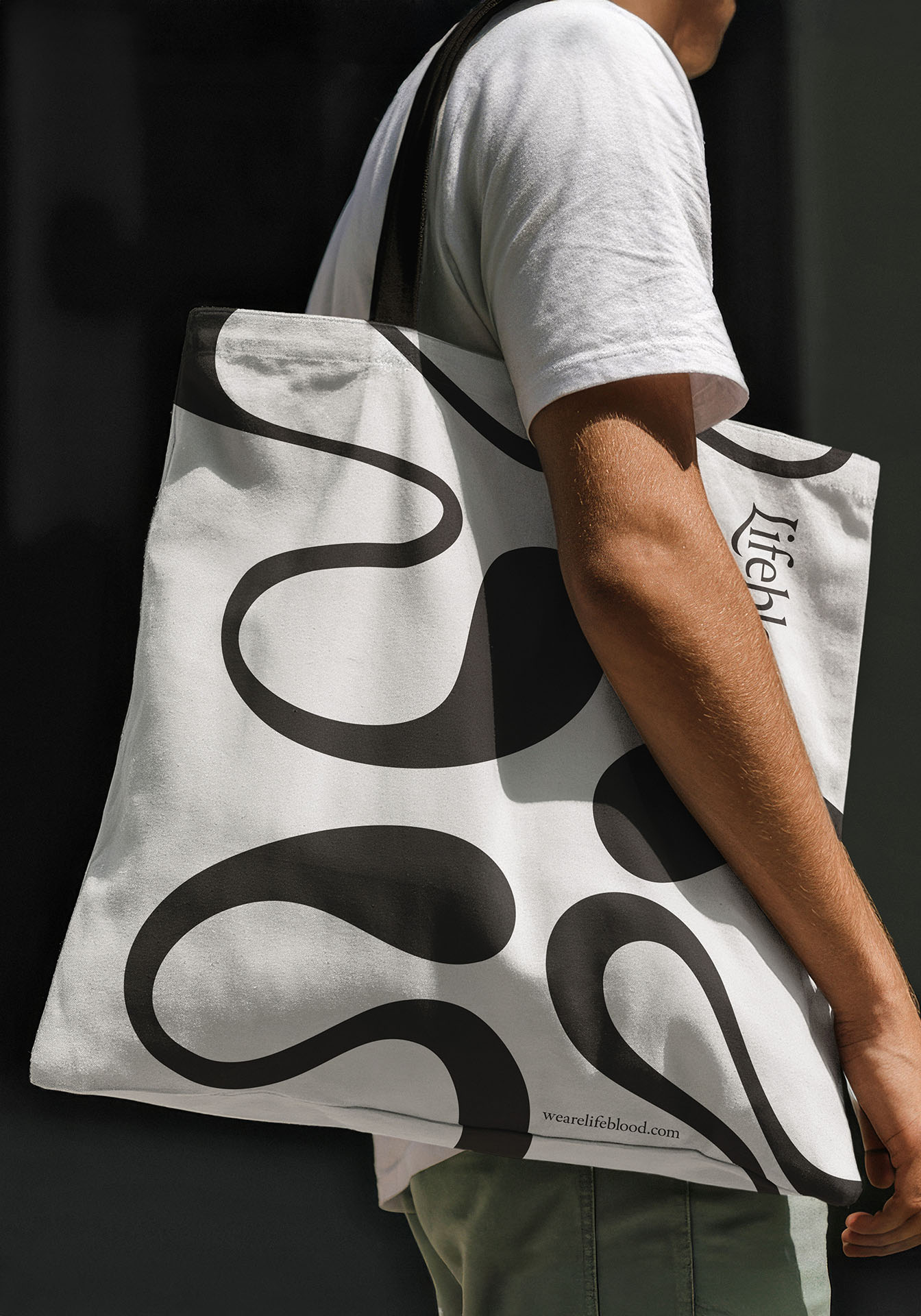 Man wearing a white t-shirt with a tote bag on his right shoulder featuring the Lifeblood branding.