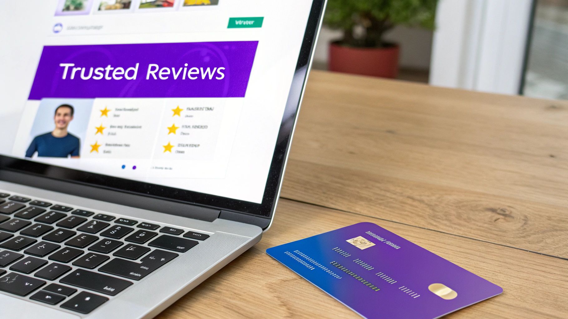 A laptop displays 'Trusted Reviews' with star ratings, beside a purple credit card on a wooden desk.