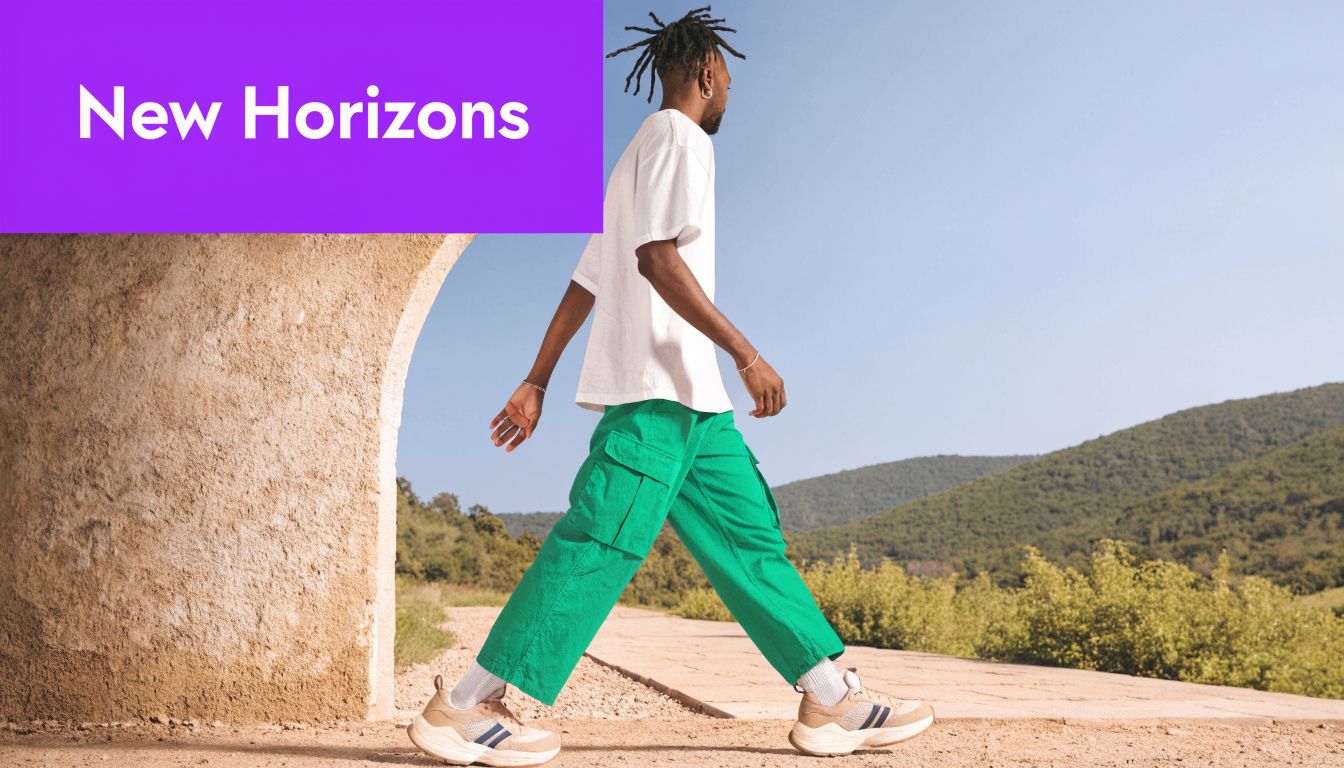 A man with dreadlocks wearing a white shirt and green cargo pants walking through an outdoor archway.
