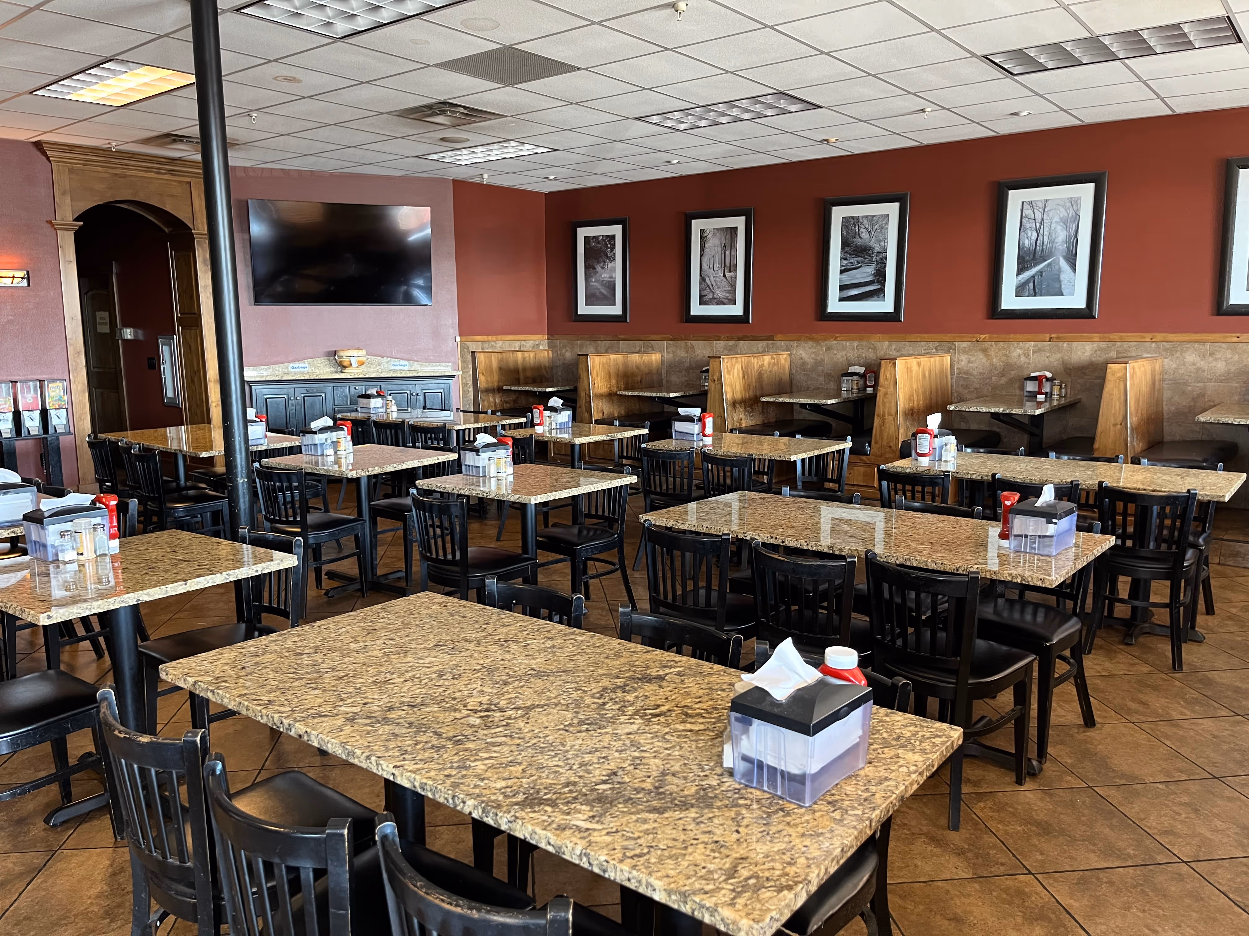 Empty restaurant dining area with granite tables, black chairs, booth seating, and framed black-and-white photos.