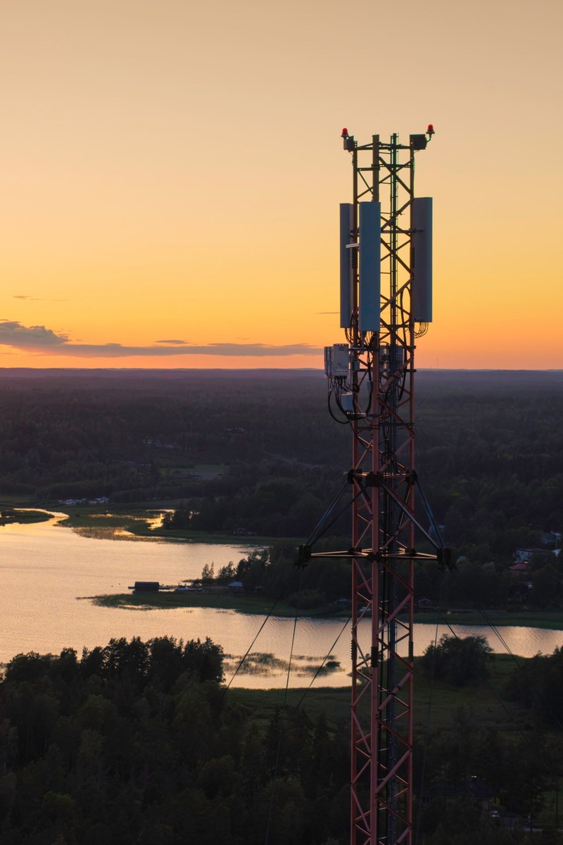 Cell tower with 5G antennas above a lake and forest at sunset