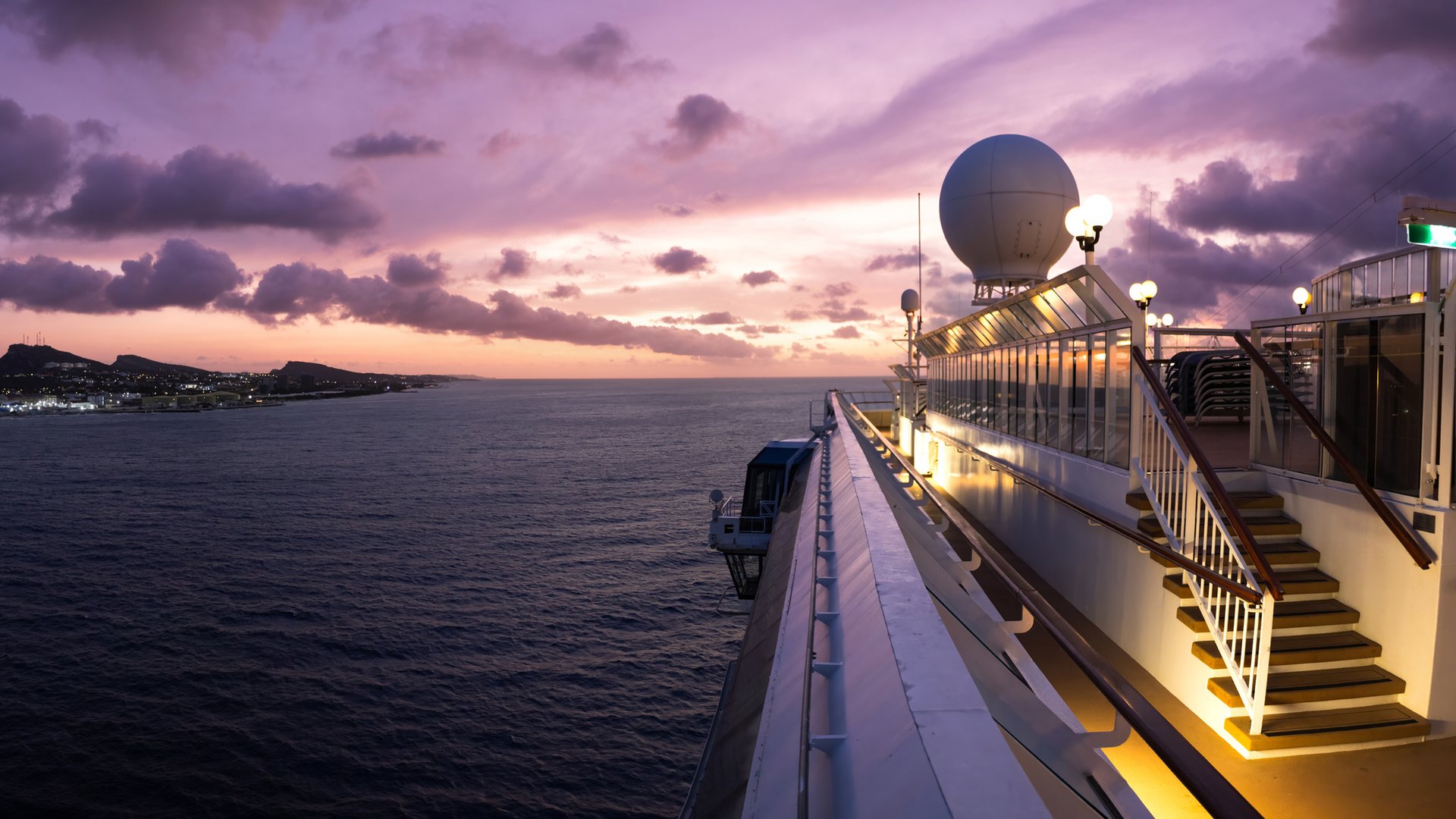Cruise ship deck with a satellite dome at sunset, overlooking the ocean and a coastline