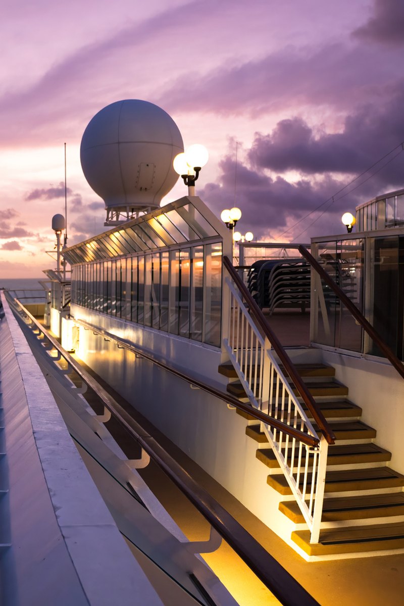 Cruise ship deck with a satellite dome at sunset, overlooking the ocean and a coastline