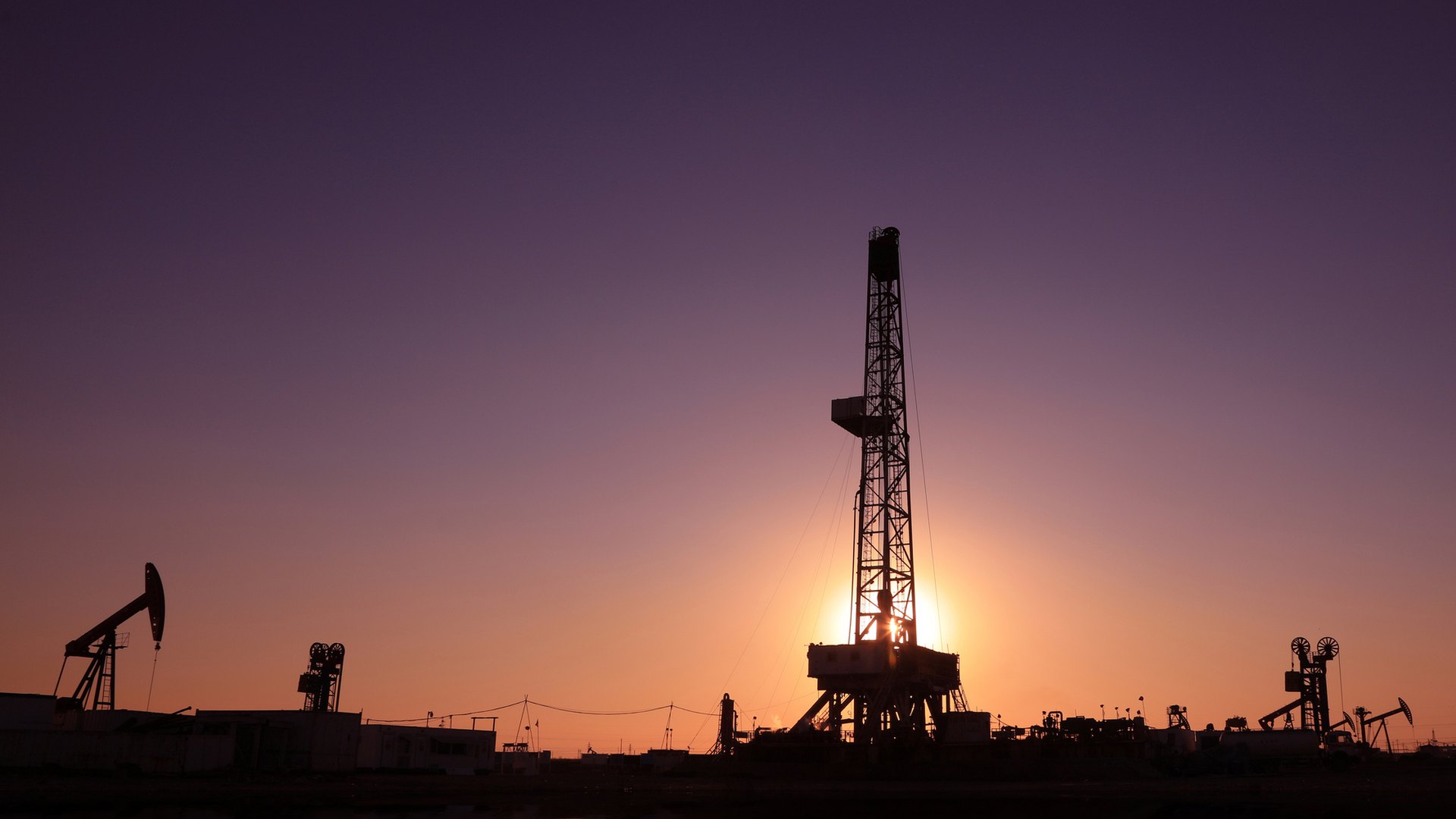 Oil drilling derrick silhouetted against a violet sunset