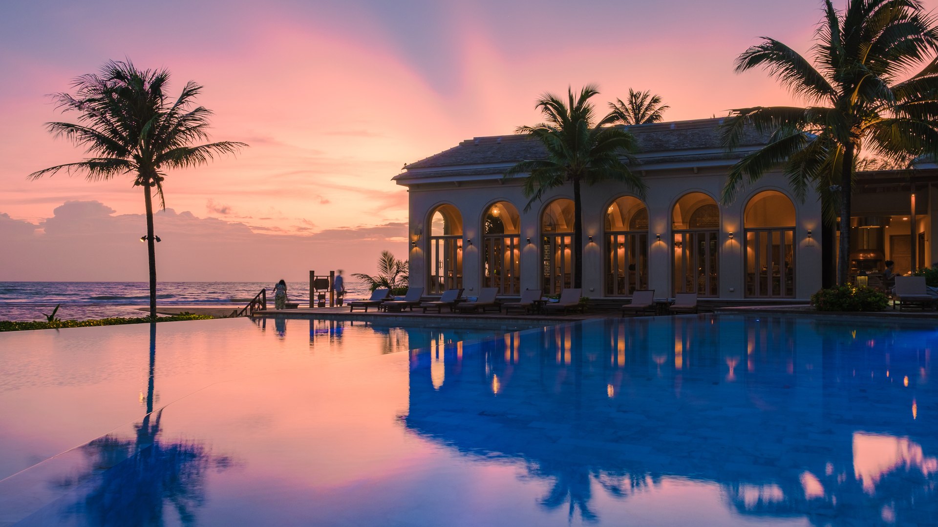 Resort with arched windows beside an infinity pool at sunset