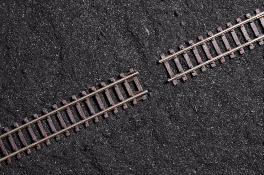 Aerial photograph of two disconnected sections of railway track on a dark surface, used as a visual metaphor for the gap between when a signal appears and when an organisation acts on it.