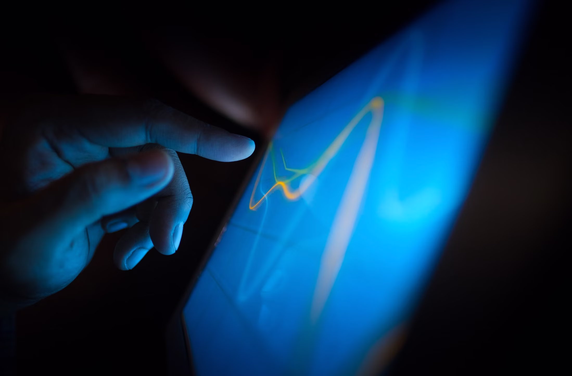 A finger reaching toward a single highlighted line on a glowing blue screen, isolating one signal from the display