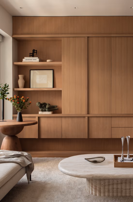 Modern living room with wooden built-in shelving, round wooden and stone coffee tables, and neutral decor.