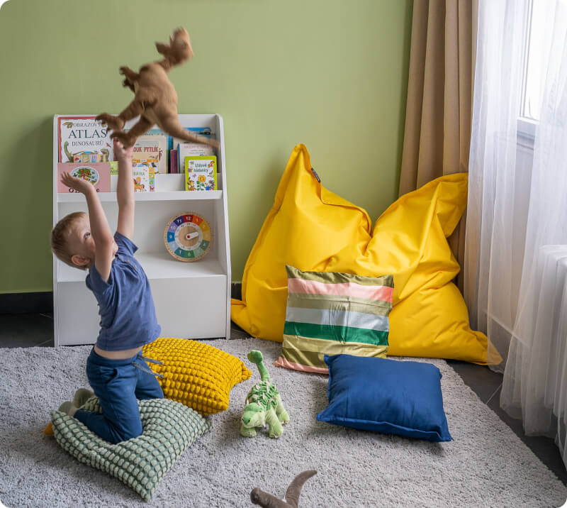 Malý chlapec hraje si s plyšovým dinosaurem v barevně zařízeném dětském pokoji.