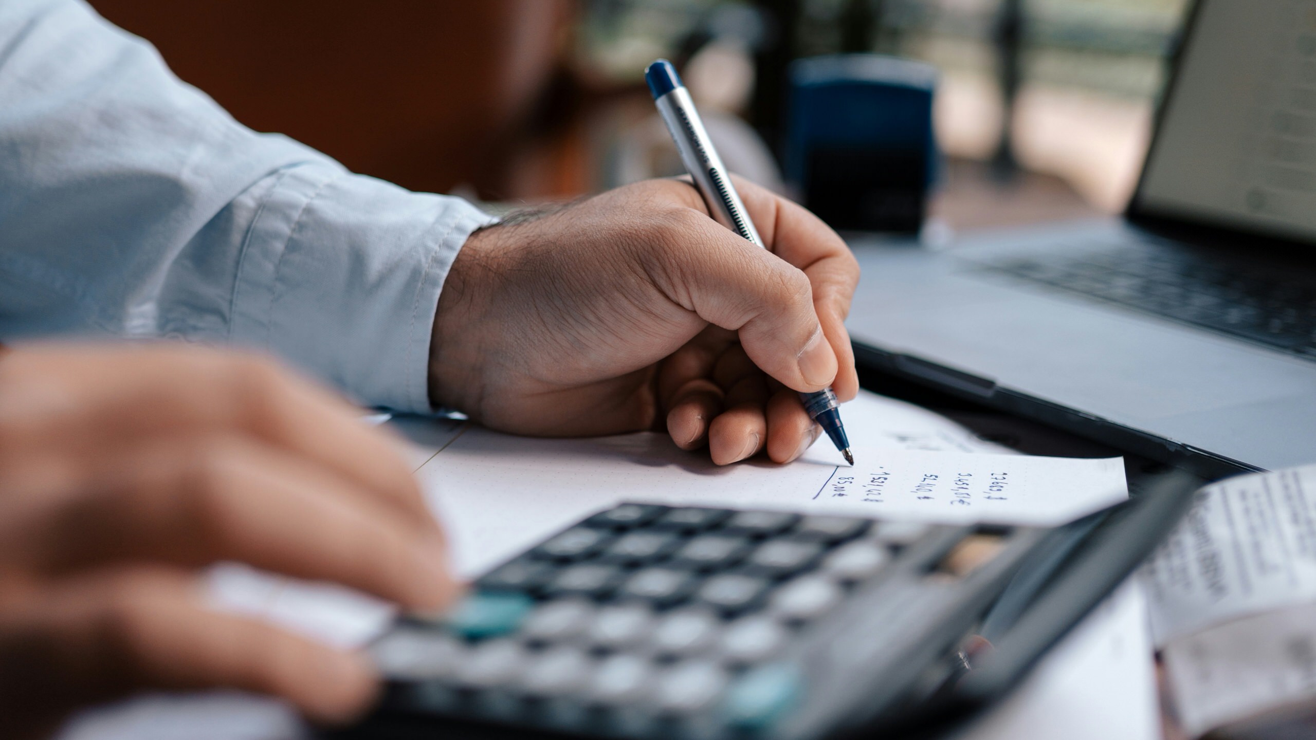 A dentist working through some accounting using a pad of paper, pencil, and calculator. 