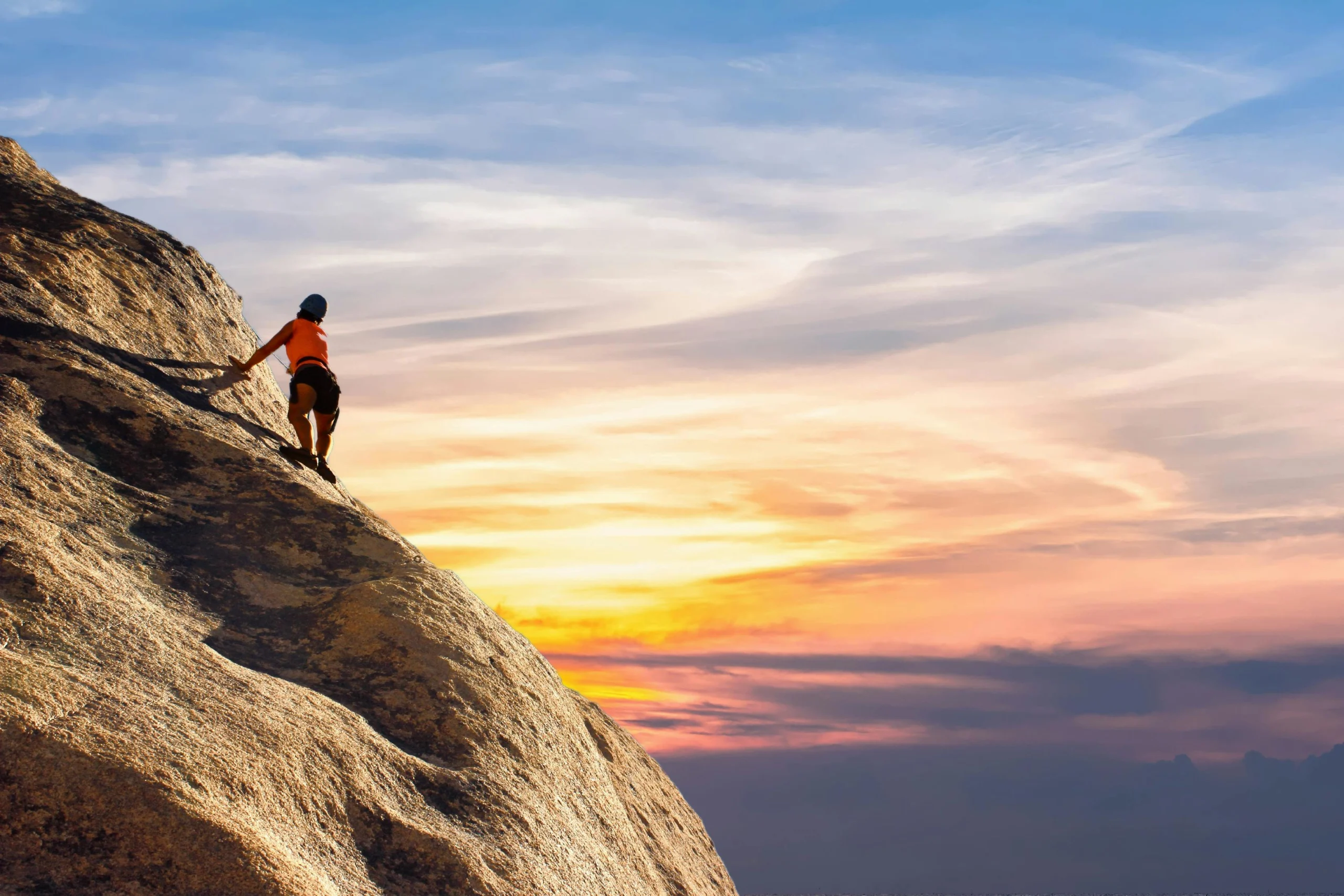 Rock climber ascending steep cliff at sunset with vibrant sky