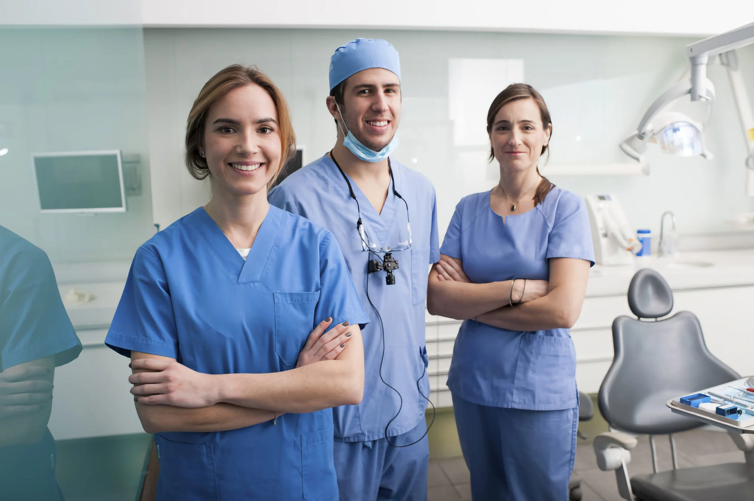 Three medical professionals in blue scrubs standing in a dental office