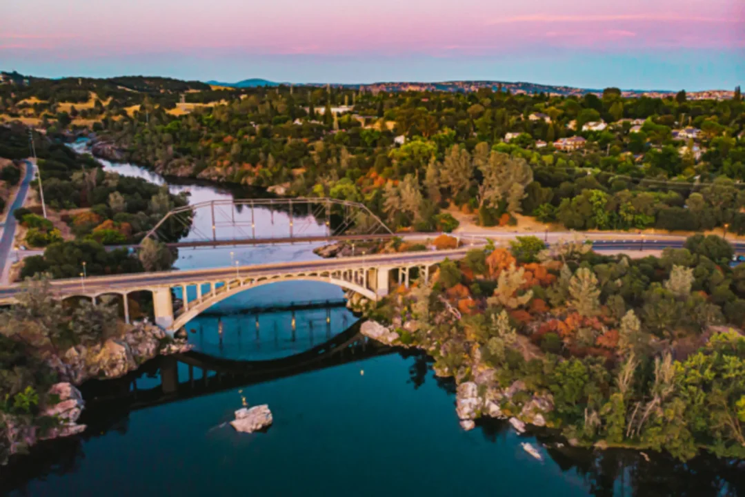 Arched bridge over blue river surrounded by autumn trees at sunset