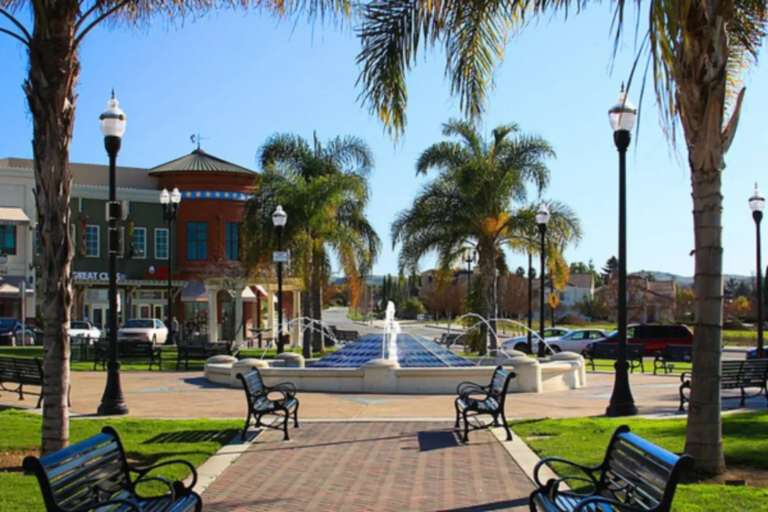 Sunny town square with fountain, palm trees, benches, and historic buildings