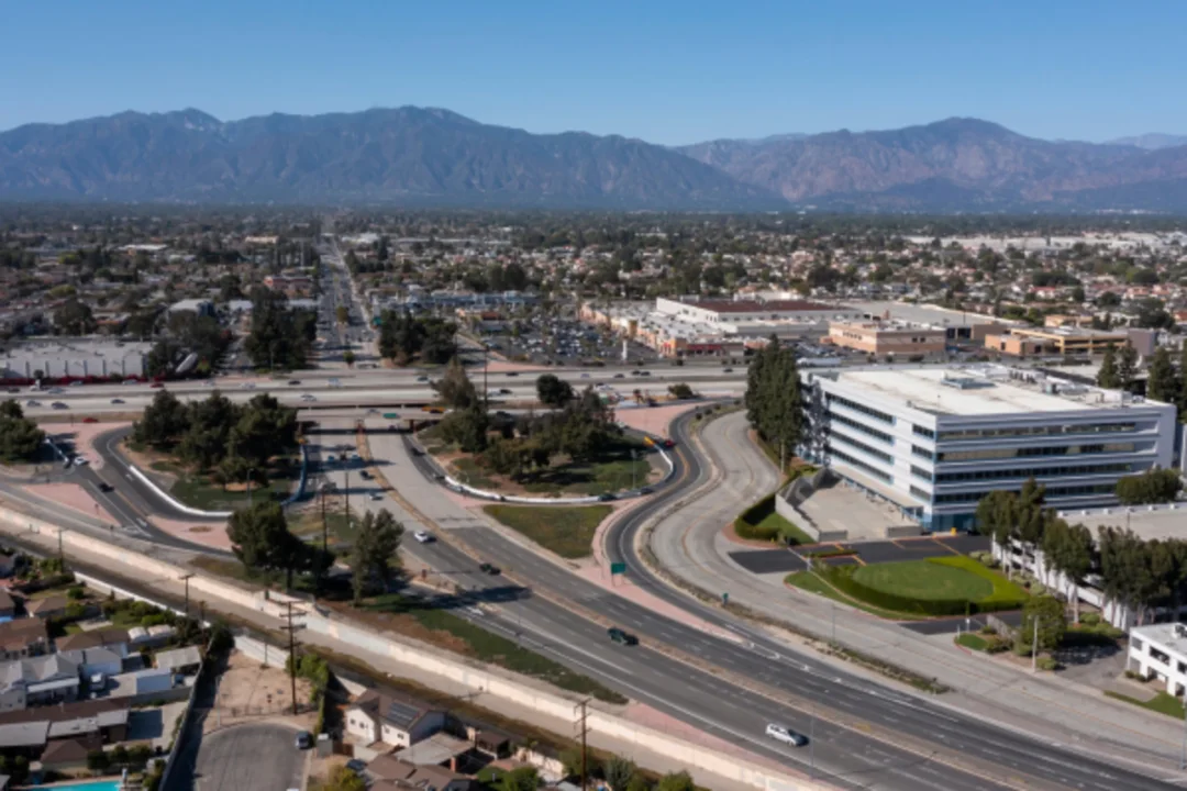 Aerial view of suburban highway interchange with mountains in background, featuring modern office building and residential areas.