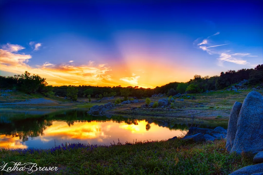 Stunning sunset reflecting in a calm lake surrounded by rocks and trees in a natural landscape setting.