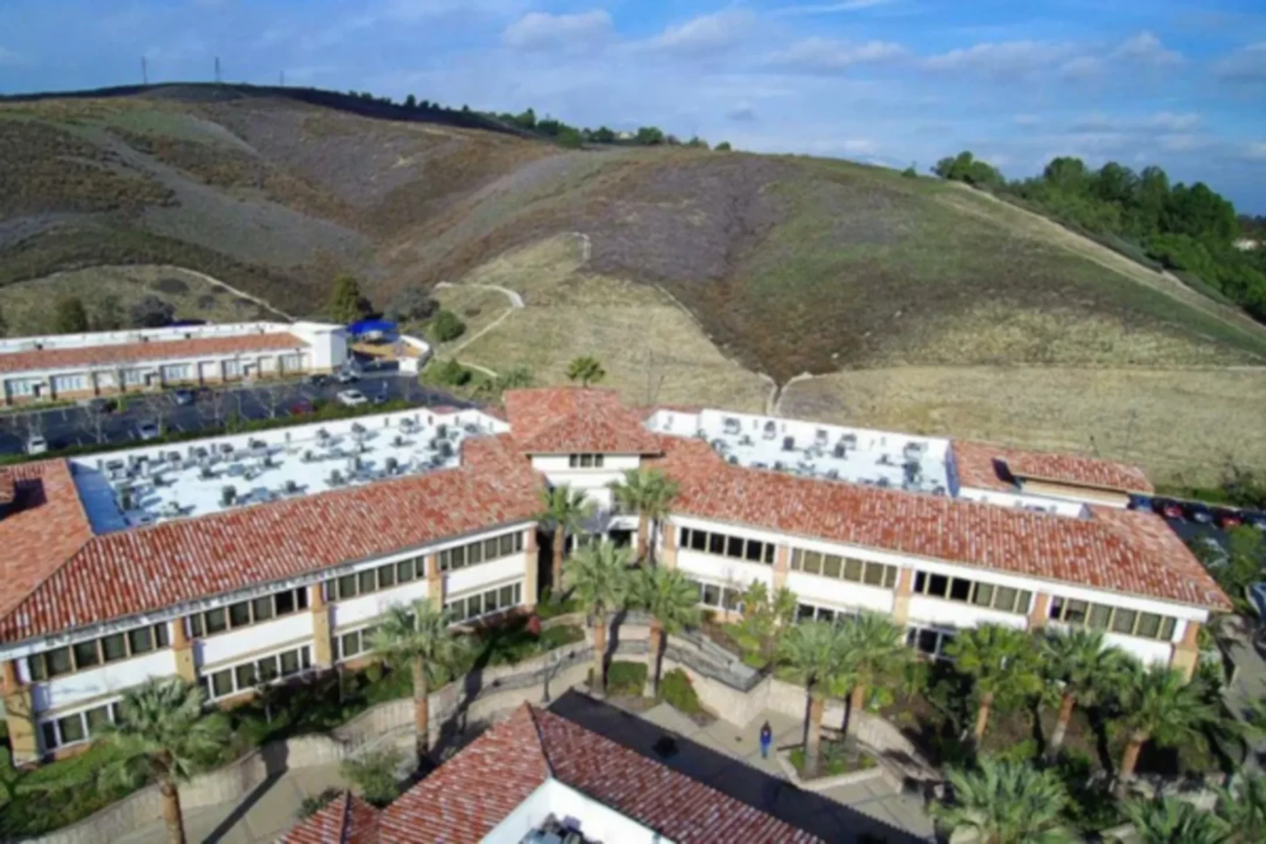 Aerial view of modern campus with red-tiled roofs and palm trees near hills