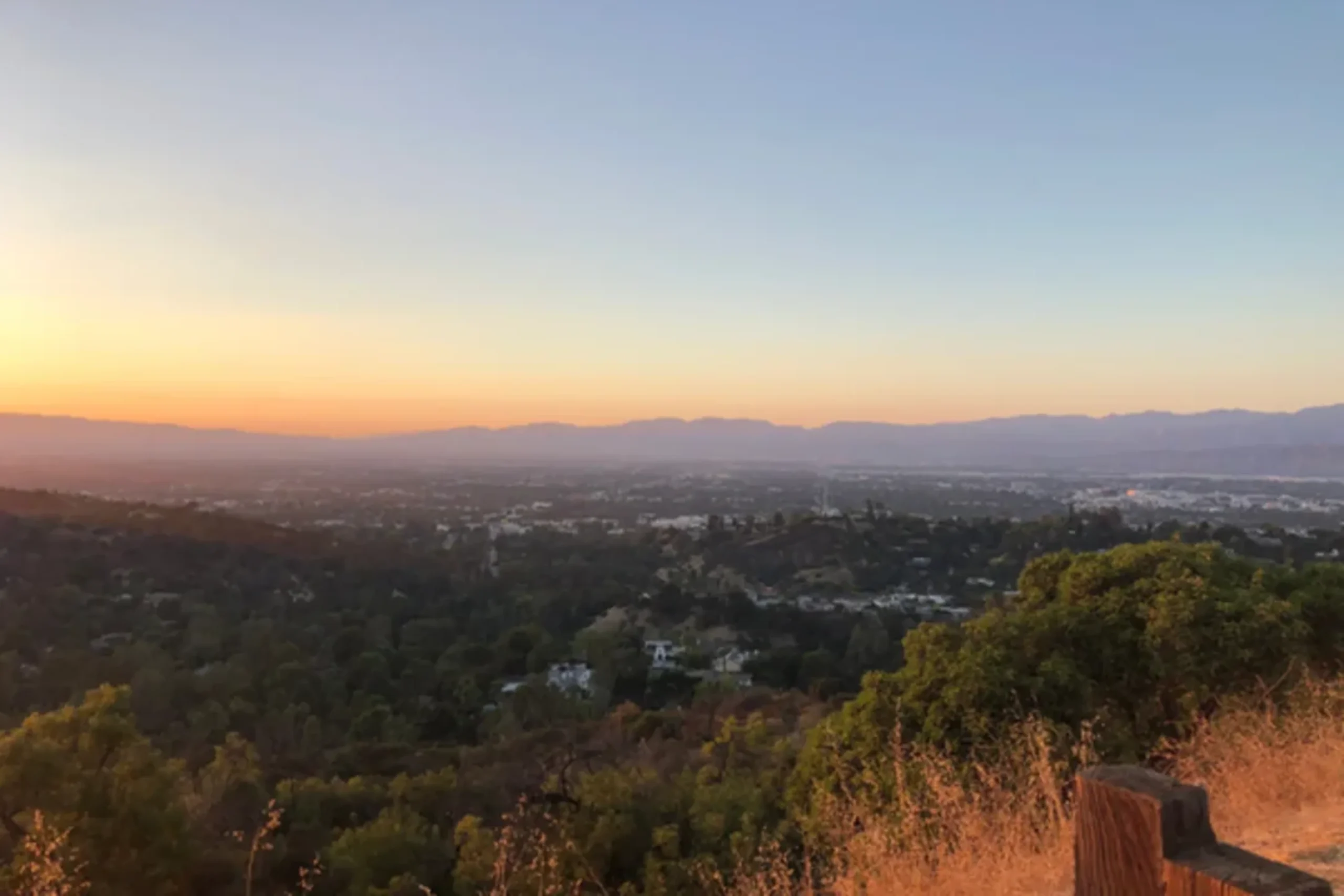 Sunset over forested landscape with distant mountains and urban sprawl