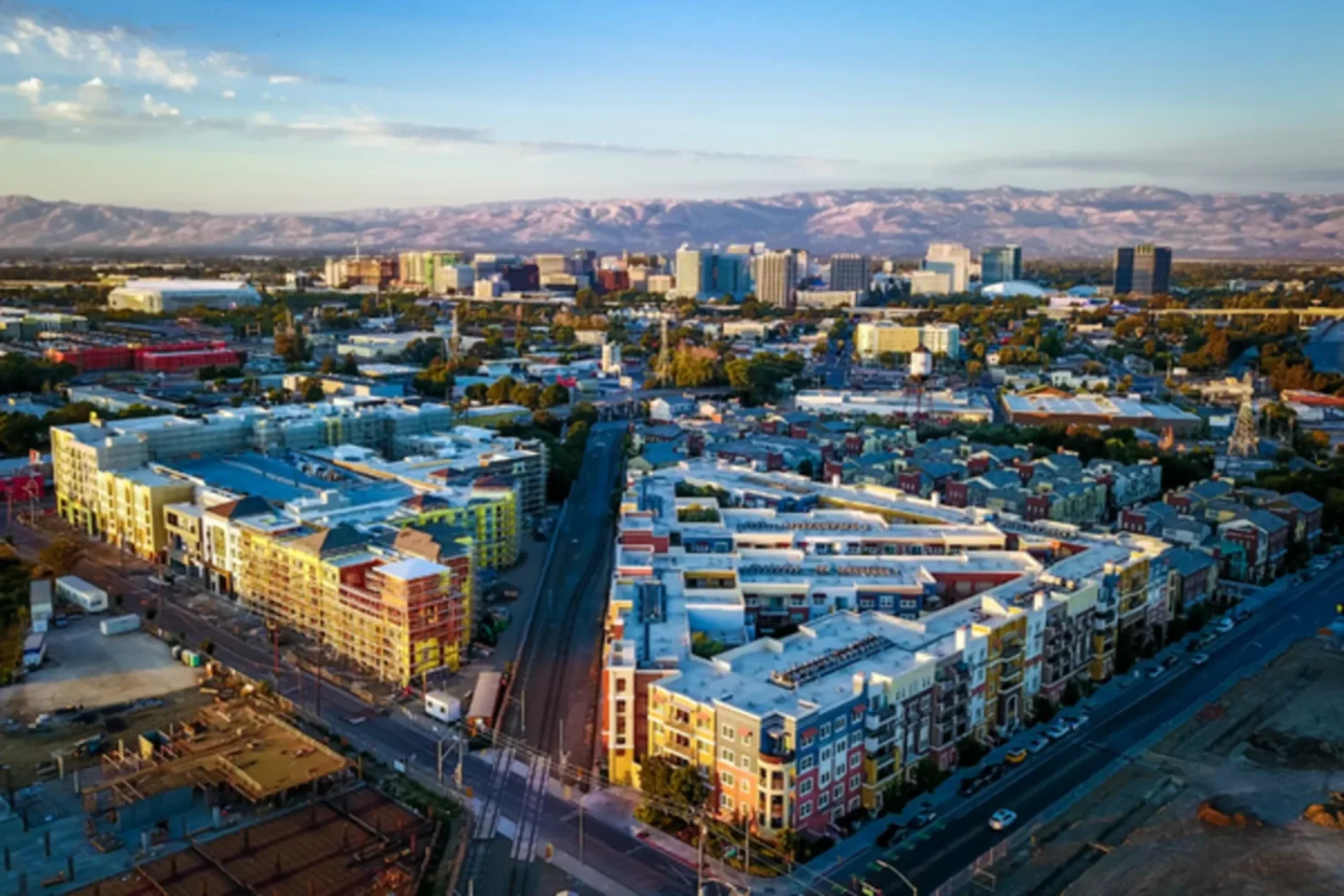 Aerial view of San Jose, California skyline with downtown buildings, colorful residential developments, and mountains in the background