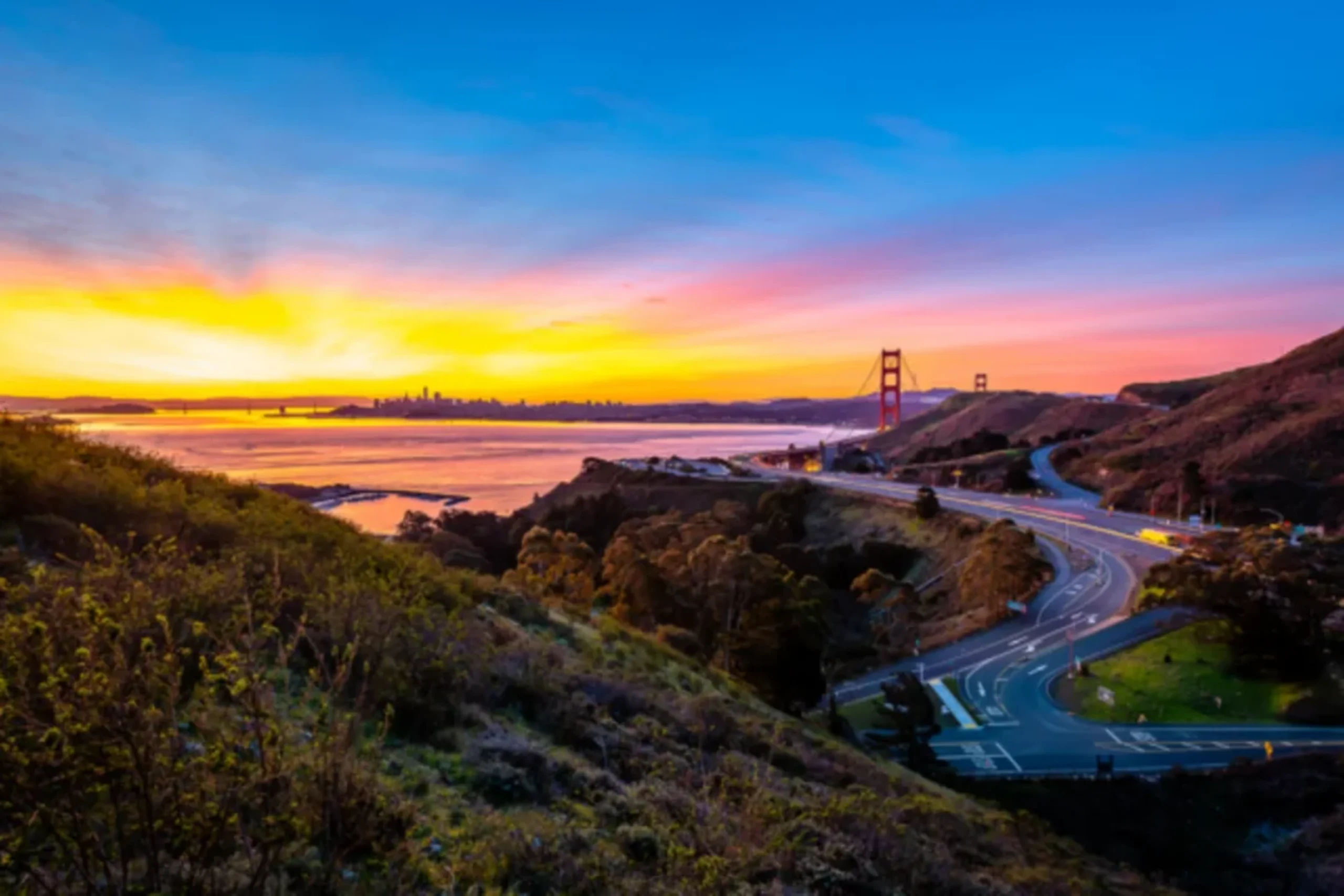 Golden Gate Bridge at sunrise with winding road and San Francisco skyline